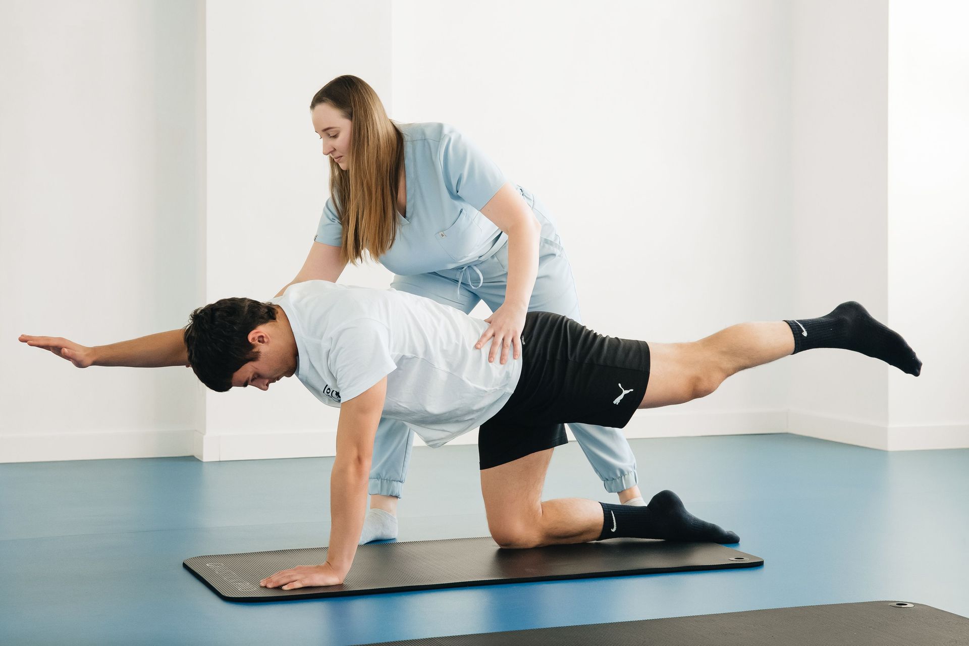 Physical therapist assisting a man doing a floor balance exercise on a mat