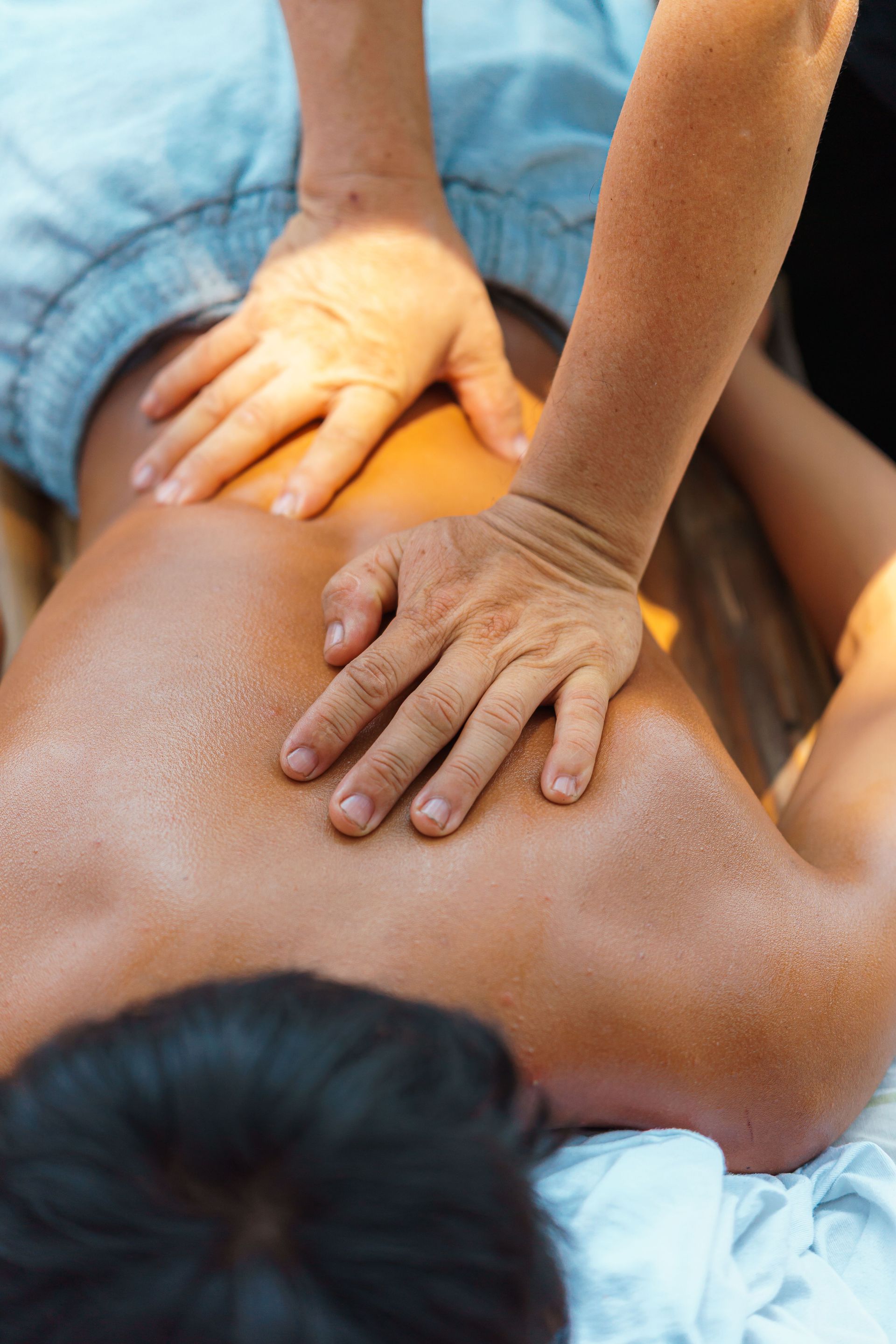 Two hands massaging a person’s bare back with orange oil on a towel.