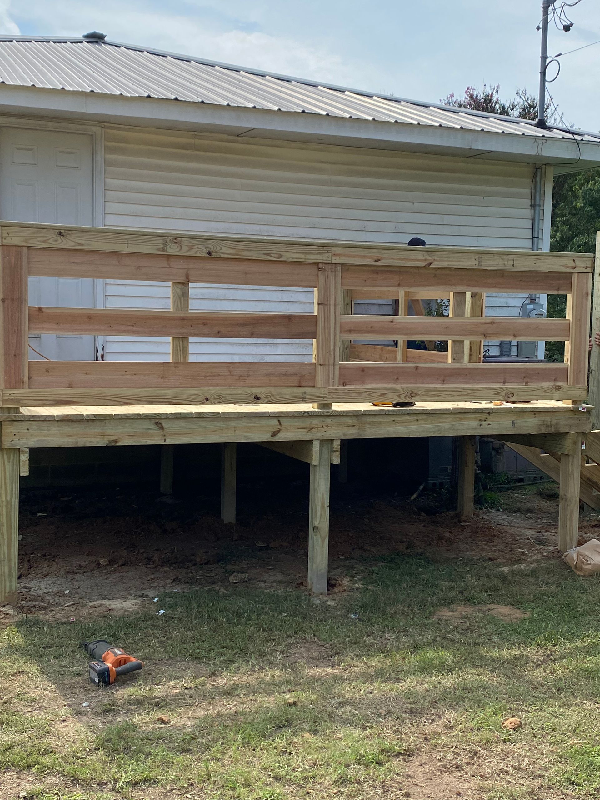 Wooden deck with a railing, attached to a house. Green grass in the yard.