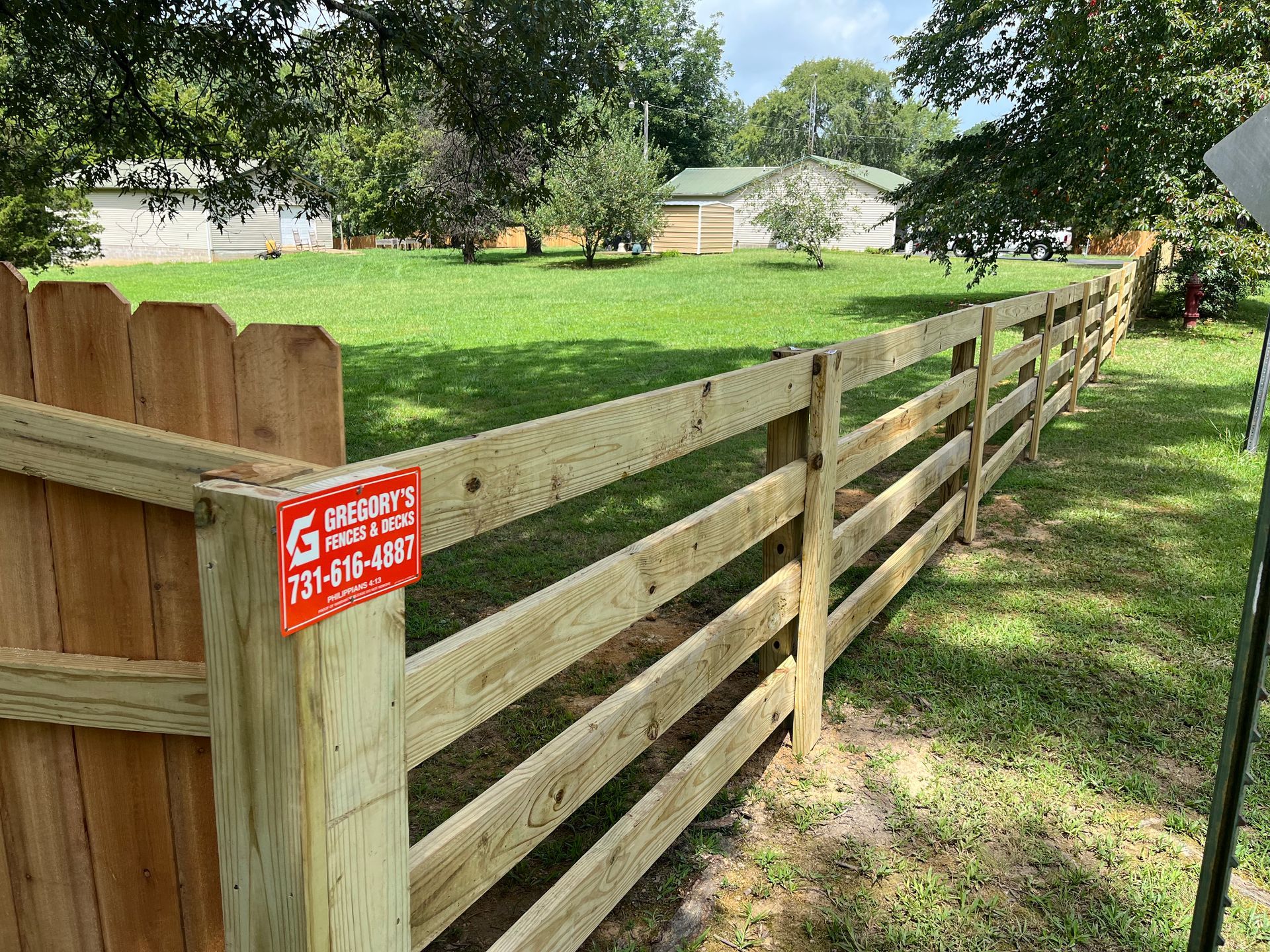 Wooden fence bordering a grassy yard. A sign with a phone number is attached to a post.