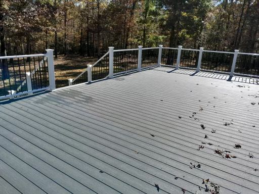 Grey deck with black railing, white posts, and fallen leaves. Forest in the background.
