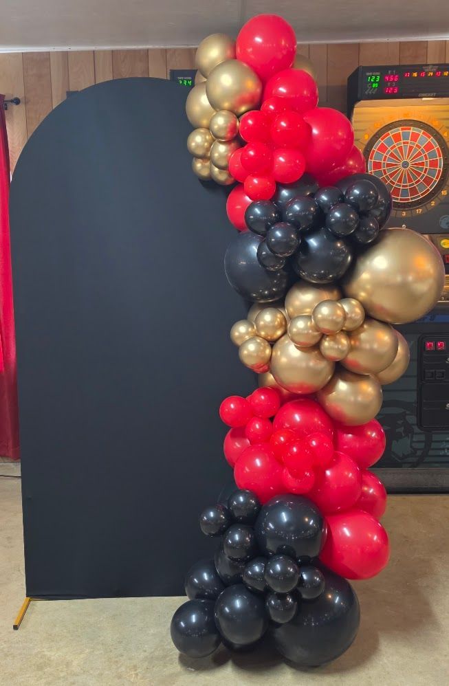 Custom black, red, and gold organic balloon garland on black arched backdrop rental for graduation event in St. Hedwig