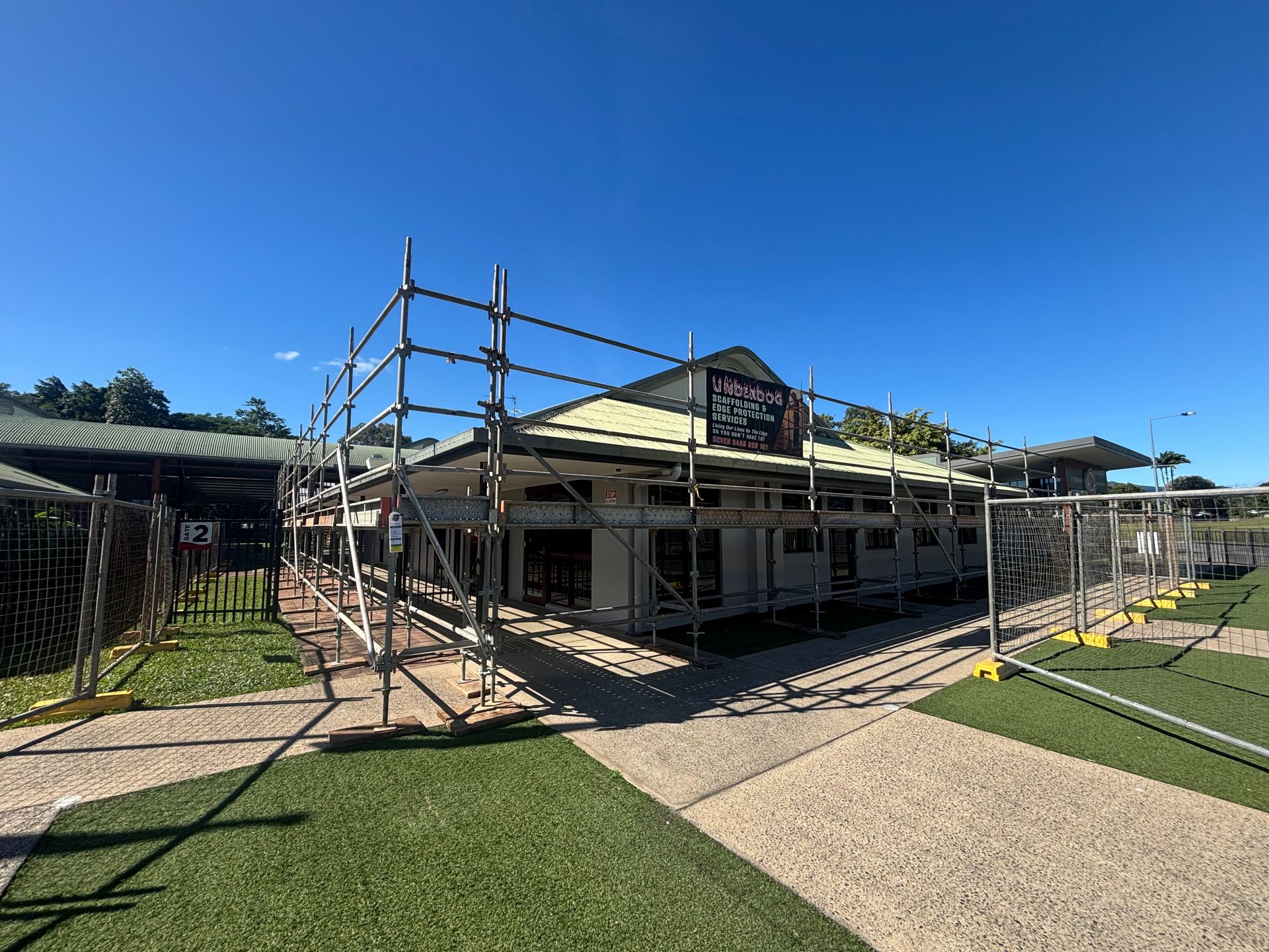 Building under construction with scaffolding, under a clear blue sky — Underdog Edge Protection in Redlynch, QLD