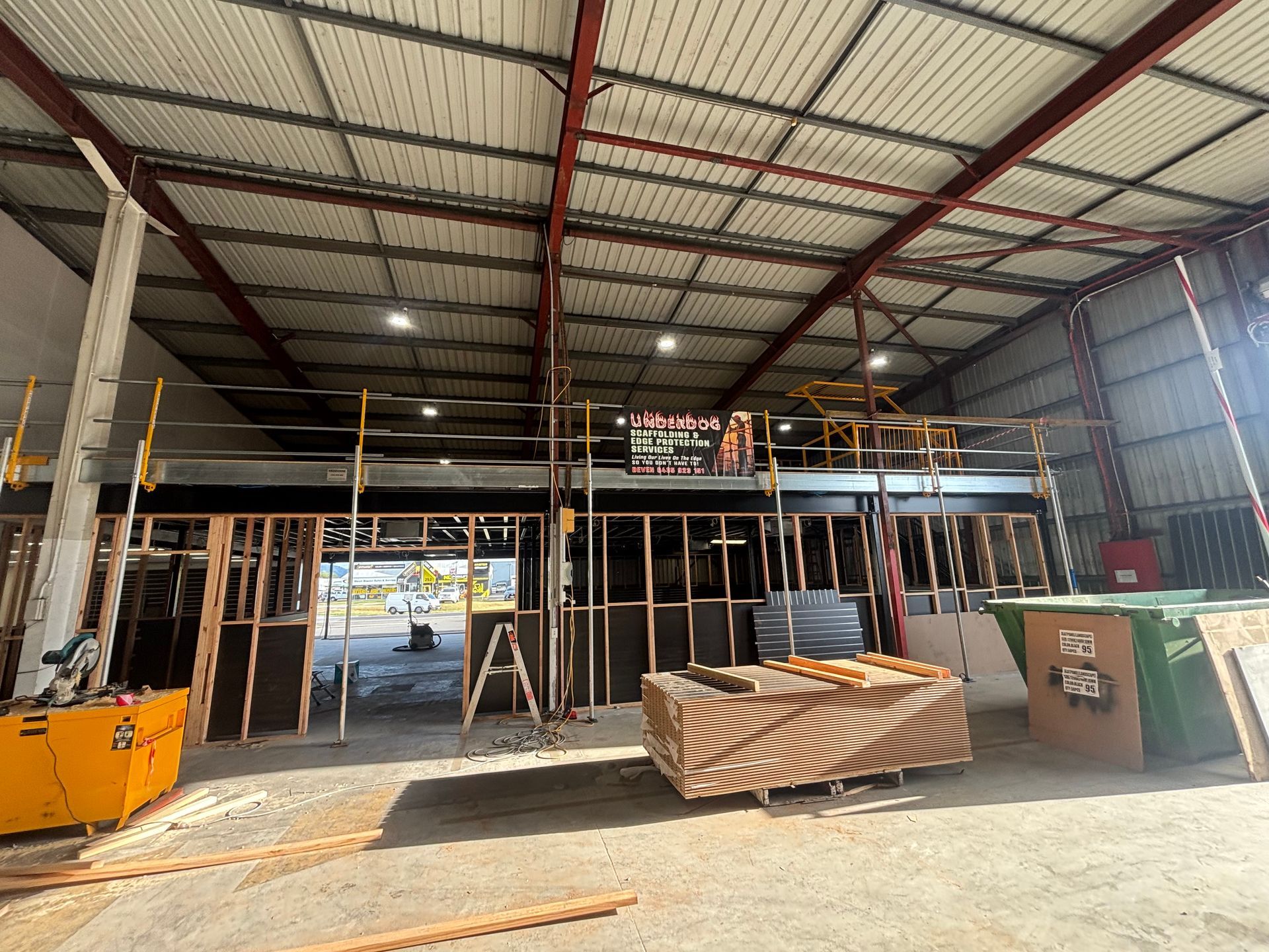 Interior of a warehouse under construction with scaffolding, ladders, and building materials under a metal roof — Underdog Edge Protection in Redlynch, QLD