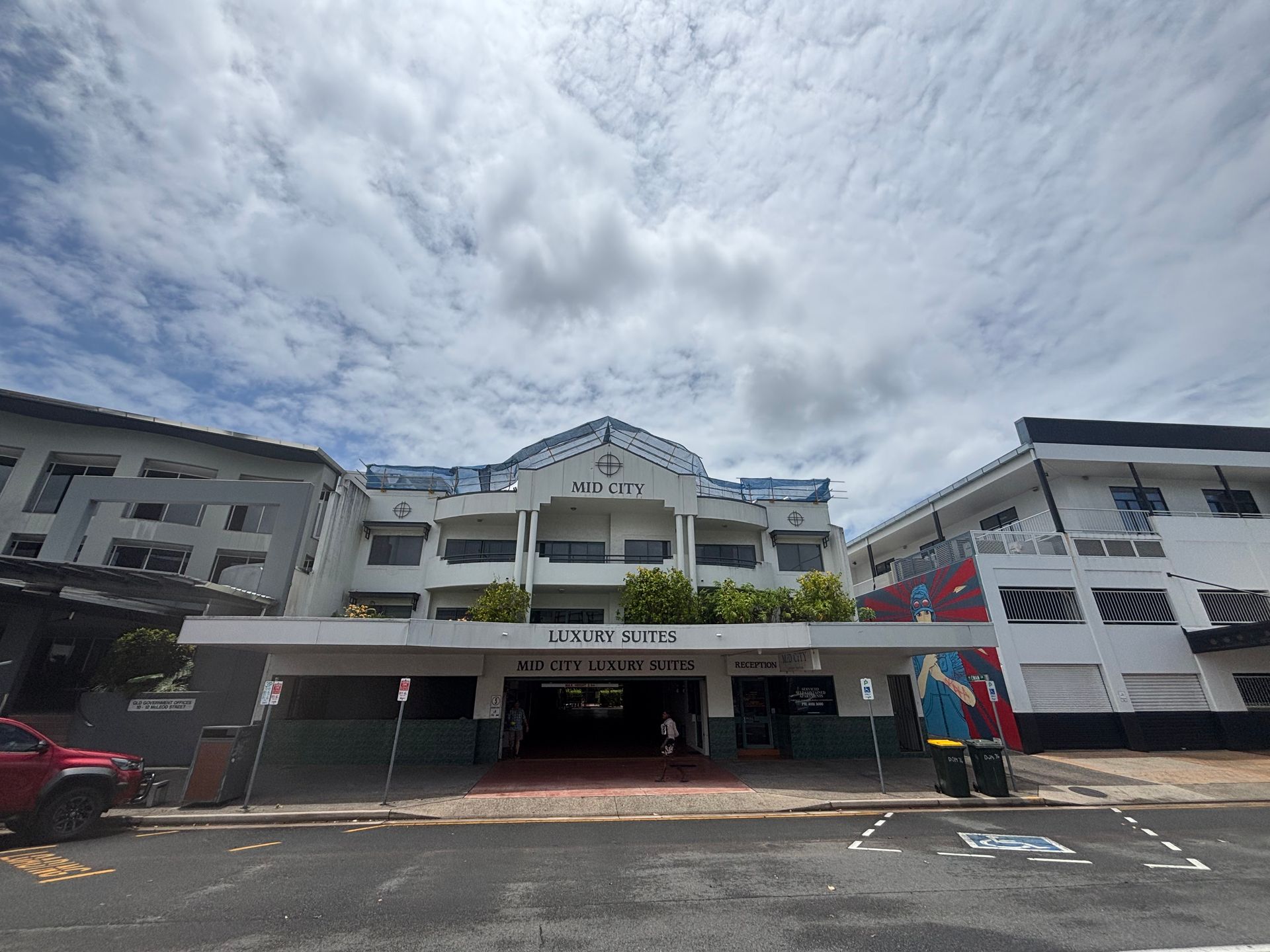 Hotel building with arched balconies and parked cars under a cloudy sky — Underdog Edge Protection in Redlynch, QLD