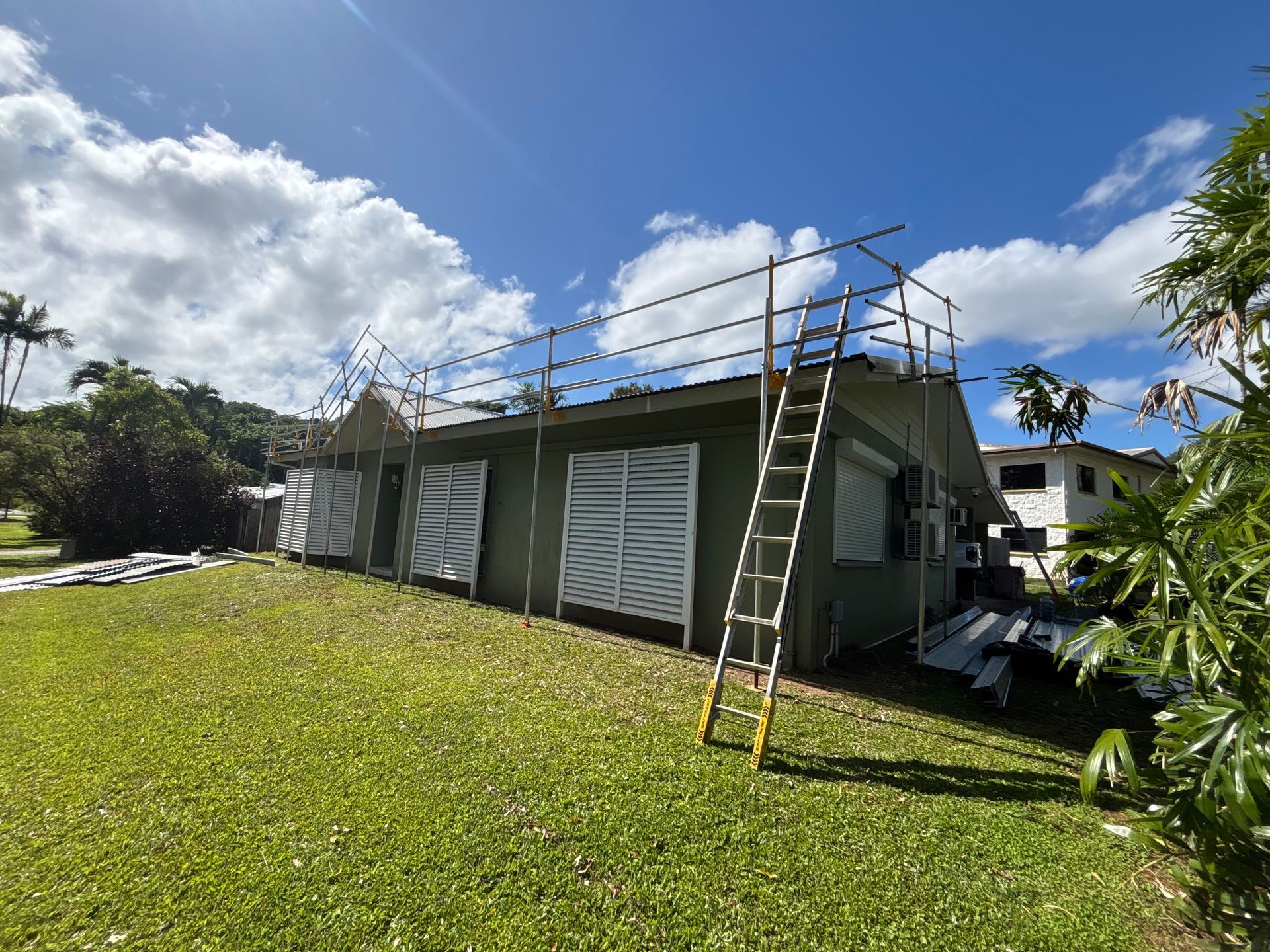 Ladder leaning on rooftop of a green house under repair, with scaffolding and a blue sky overhead — Underdog Edge Protection in Redlynch, QLD