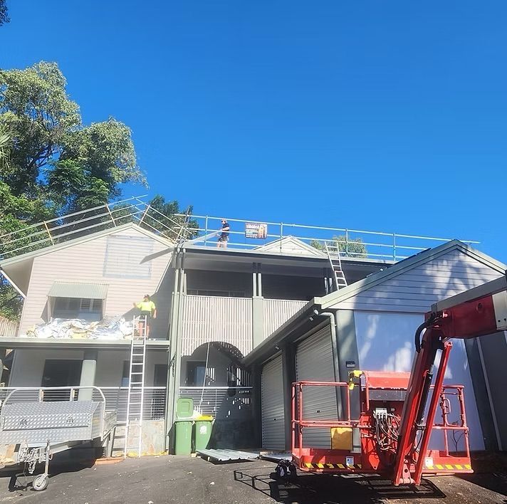 House exterior with roof repairs, a red lift, and workers on the roof under a clear blue sky — Underdog Edge Protection in Redlynch, QLD