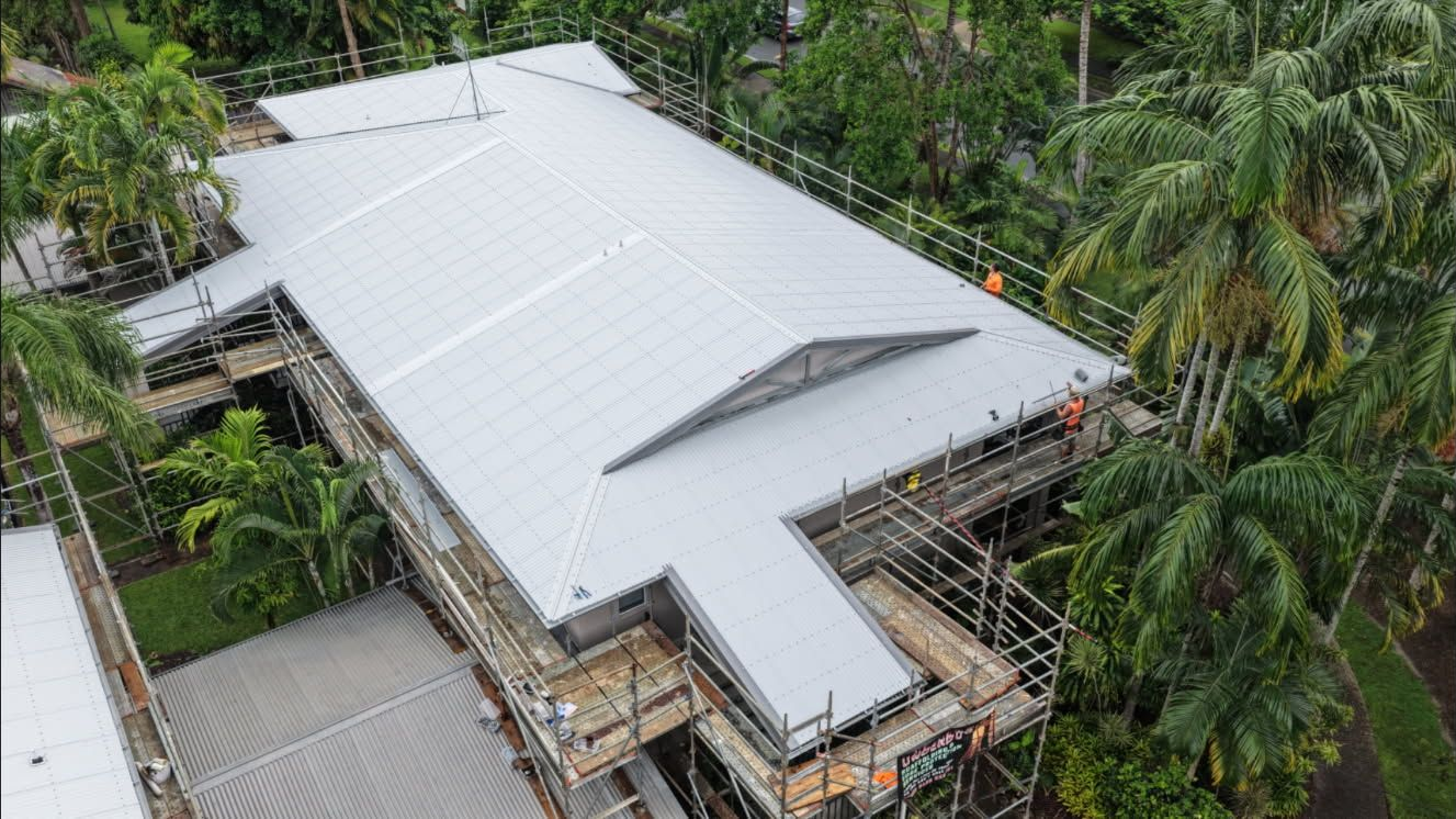 Aerial view of a white metal roof under construction, surrounded by scaffolding and dense green trees — Underdog Edge Protection in Redlynch, QLD