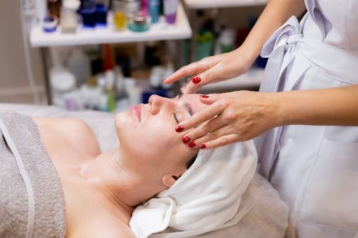 Person receiving facial treatment at a spa. Hands massaging face. Towel on head.