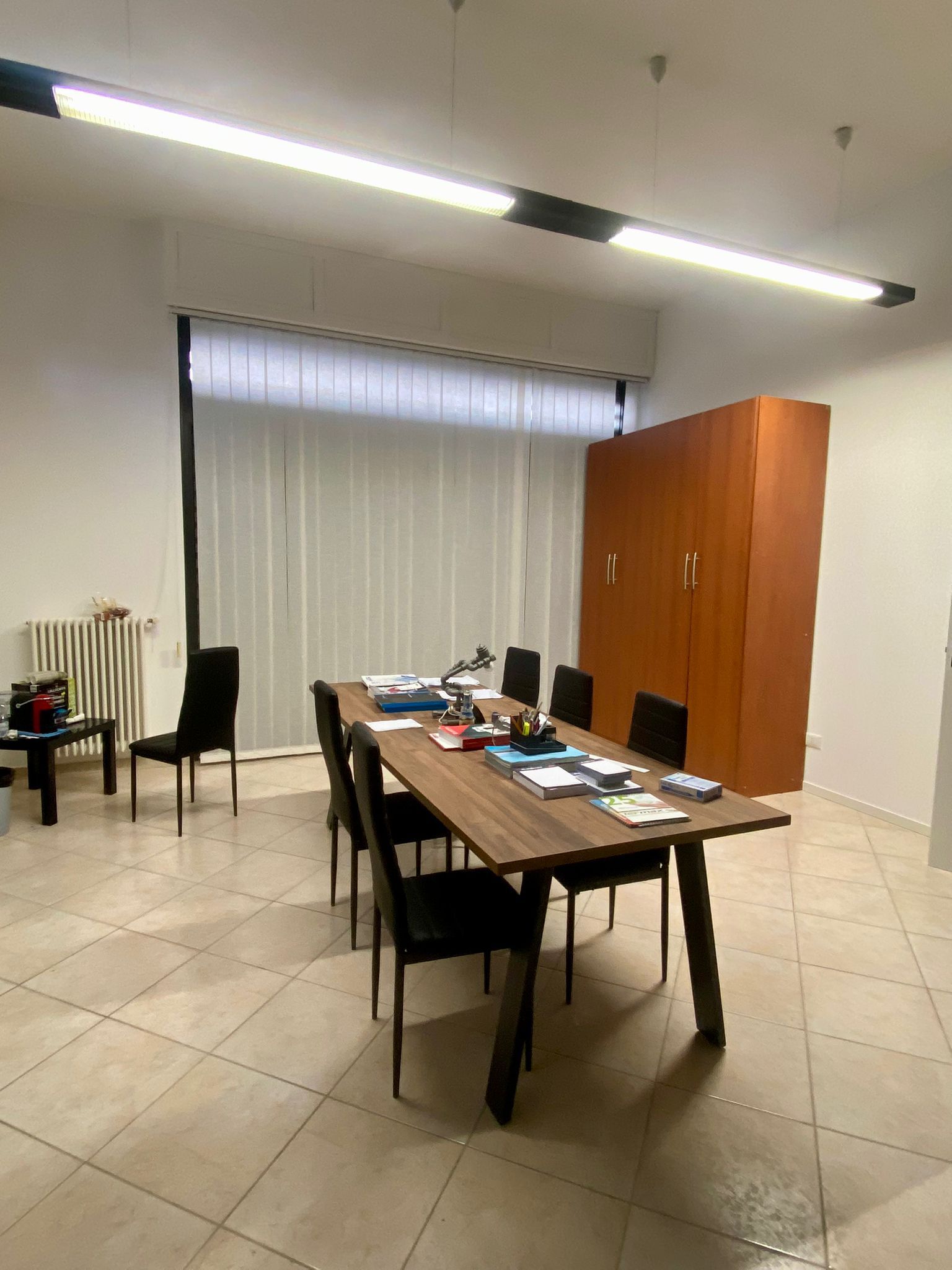 Una sala conferenze con un tavolo di legno, sedie, un mobile alto e una finestra con persiane.