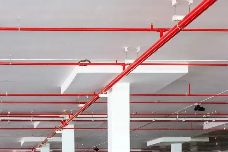 Tubi rossi degli irrigatori antincendio su un soffitto bianco in un edificio.