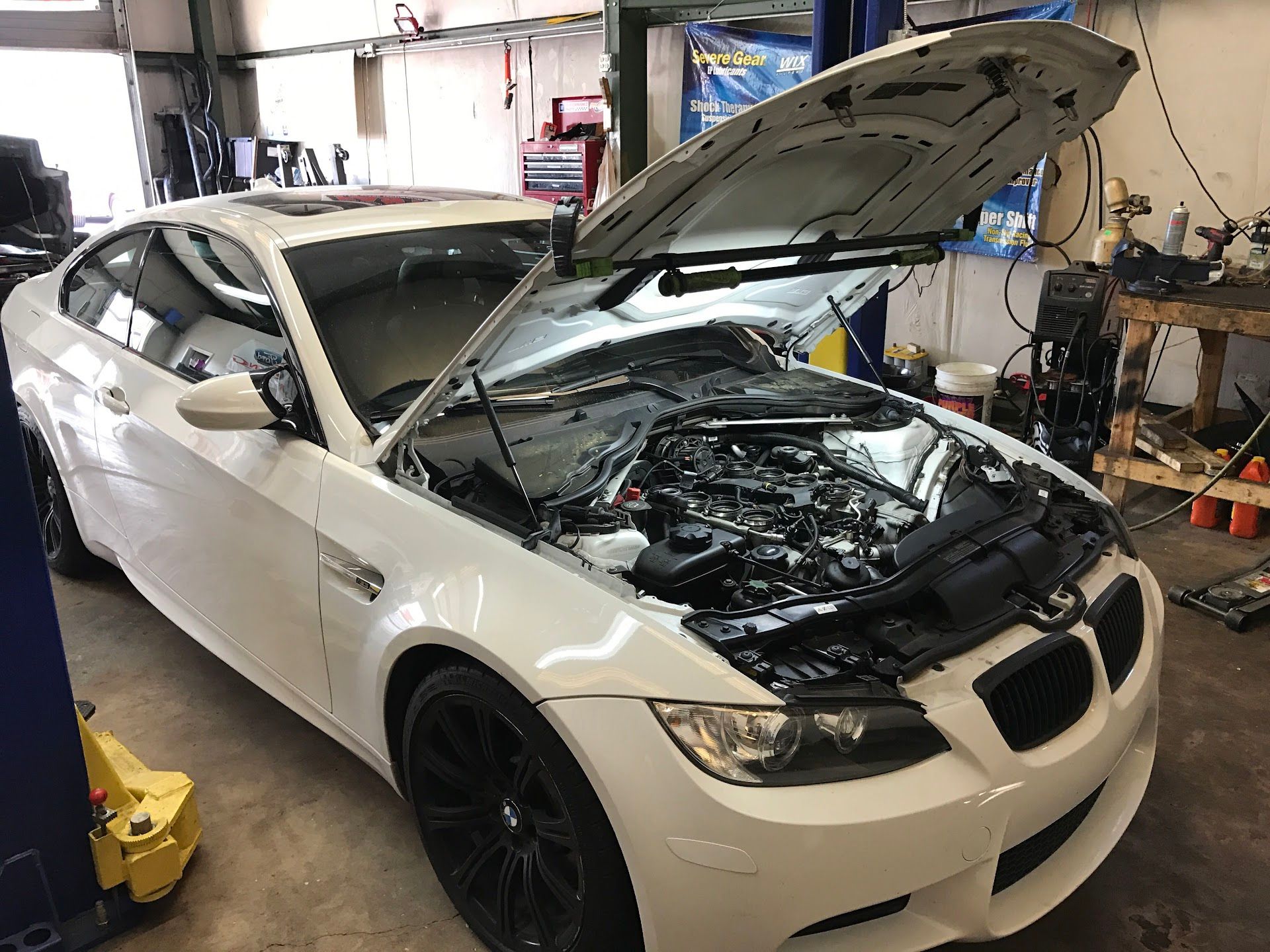 White BMW coupe with hood open in a garage, undergoing service. | YellowHammer Racing