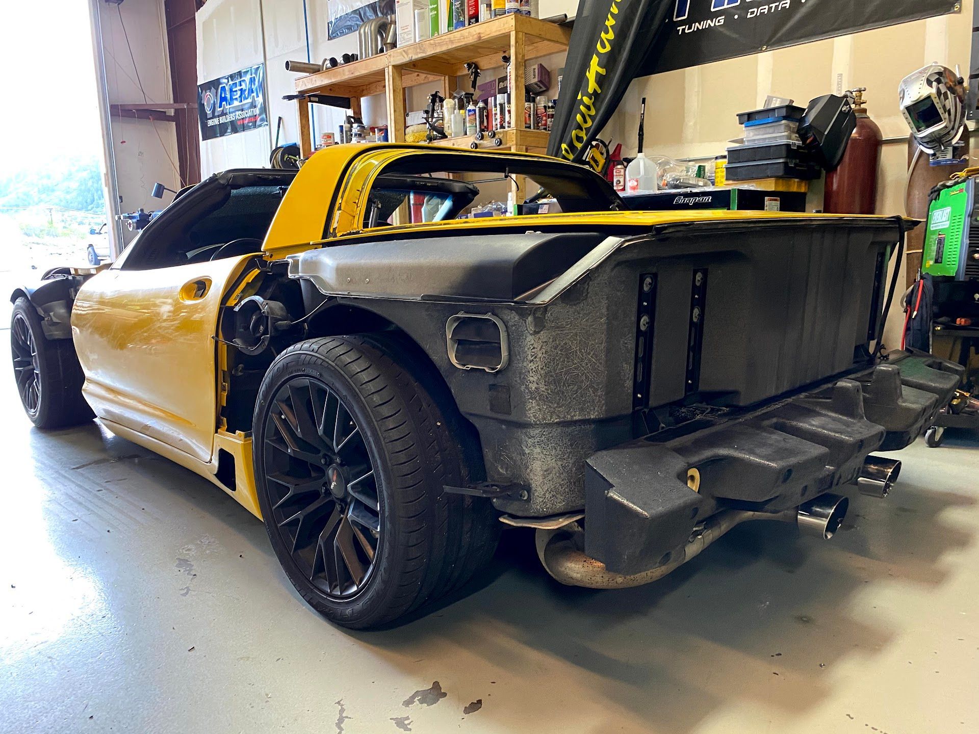 Yellow Corvette under repair, black wheels, rear bumper removed in a garage. | YellowHammer Racing