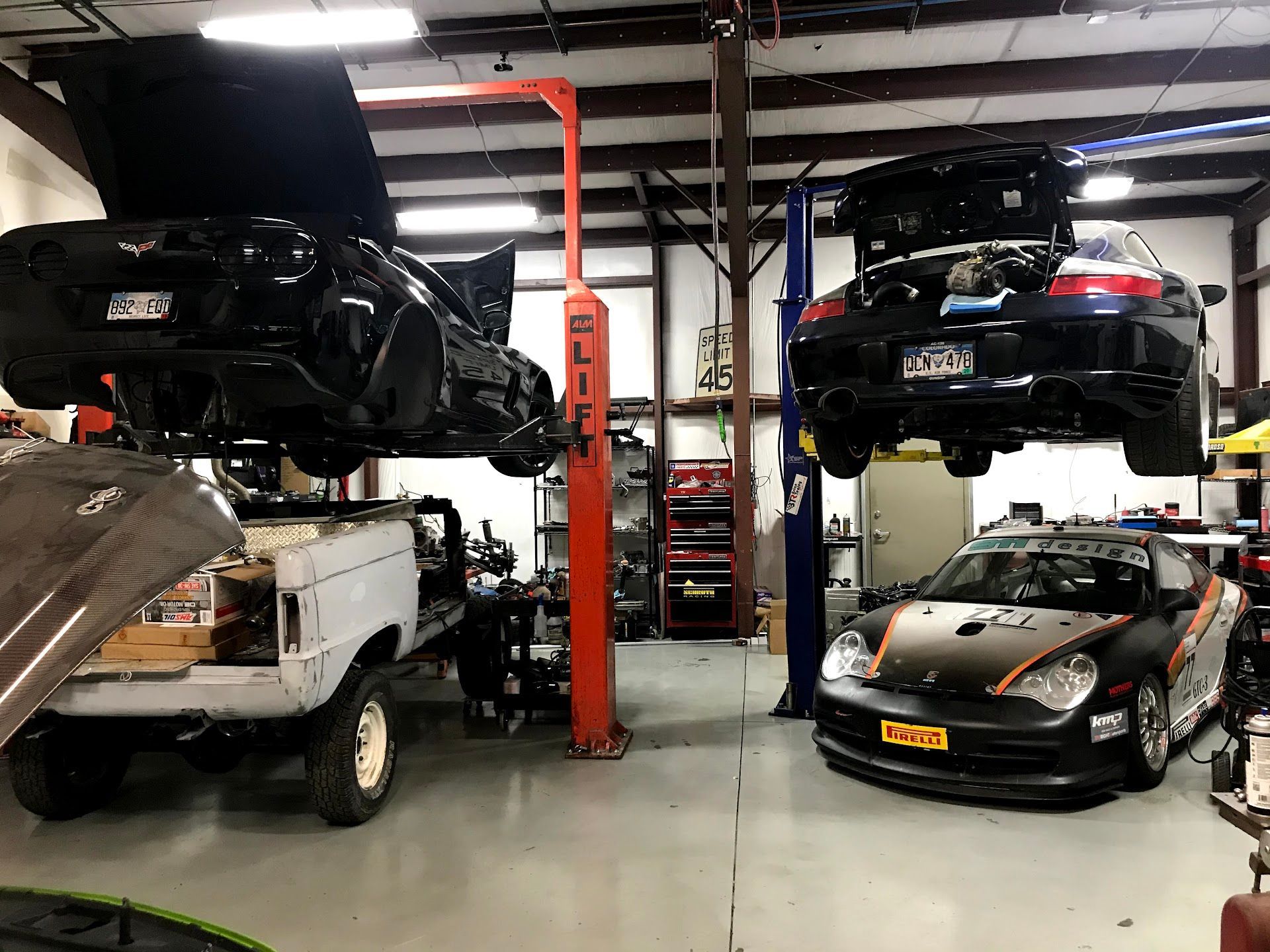 Cars on lifts in a garage: black Corvette and Porsche, old Bronco, race car. | YellowHammer Racing