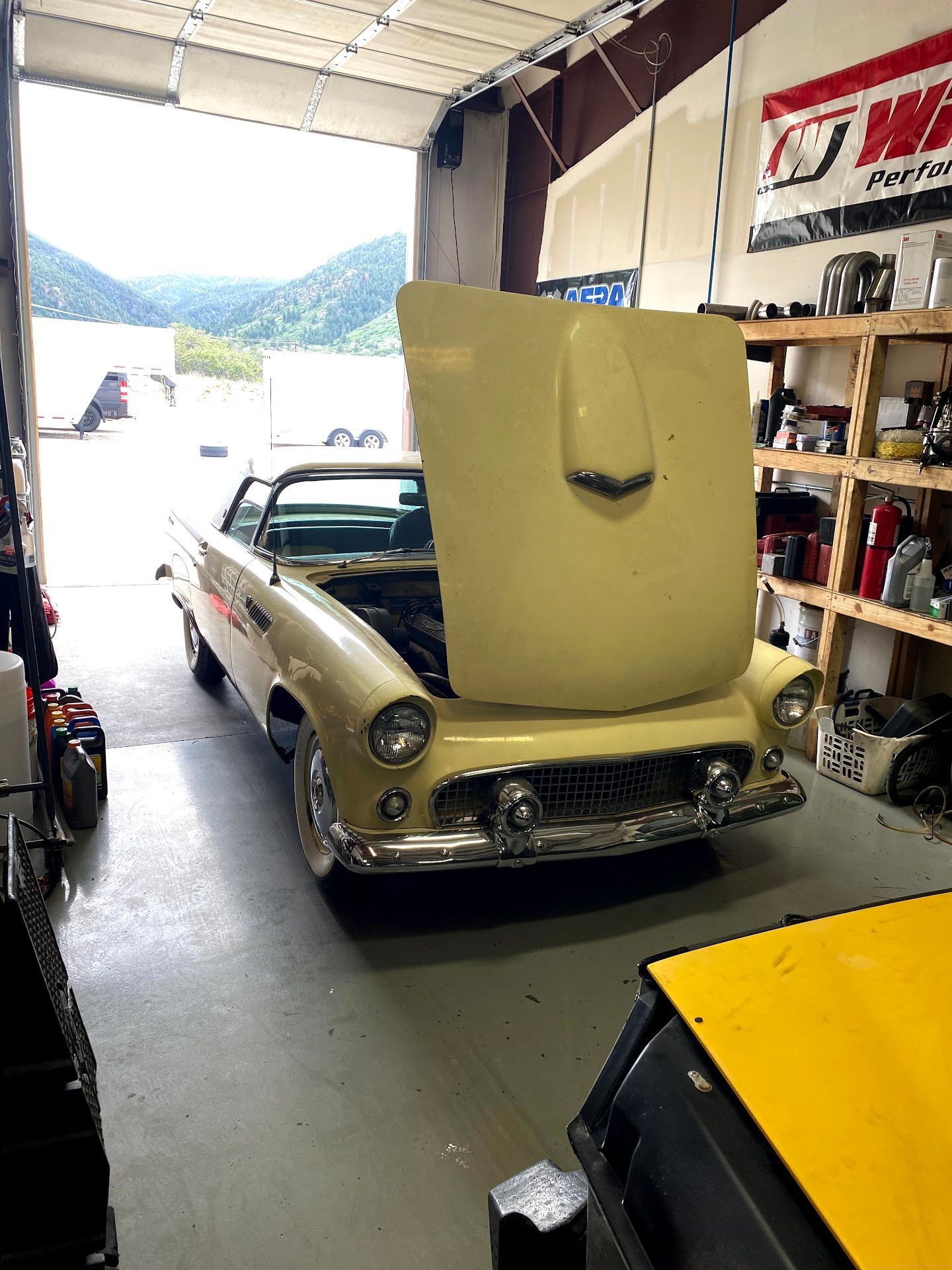 Classic yellow Ford Thunderbird with hood up in a garage, mountains visible through the open door. | YellowHammer Racing
