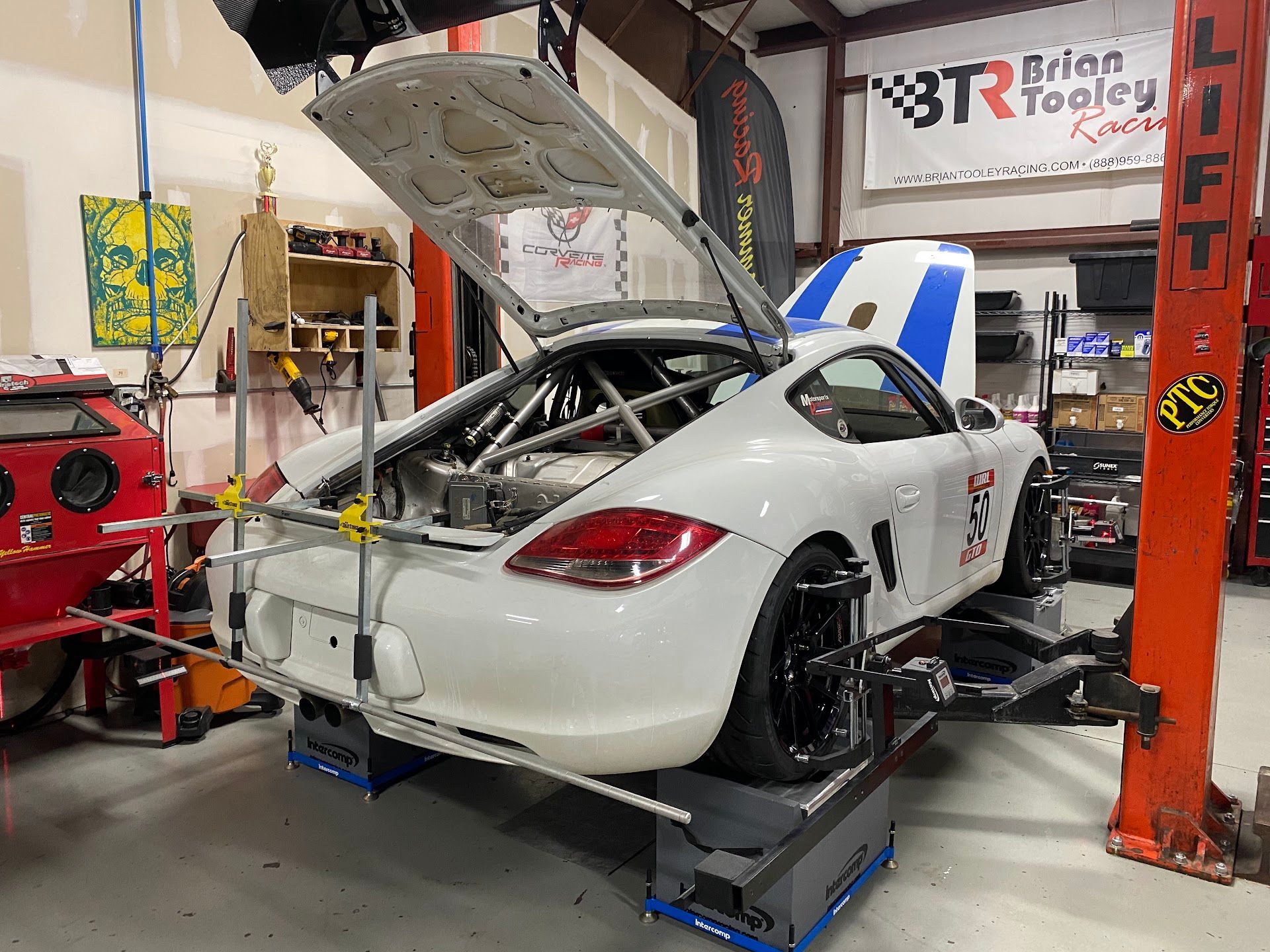 White sports car on a lift in a garage, undergoing alignment check. Rear hatch open. | YellowHammer Racing