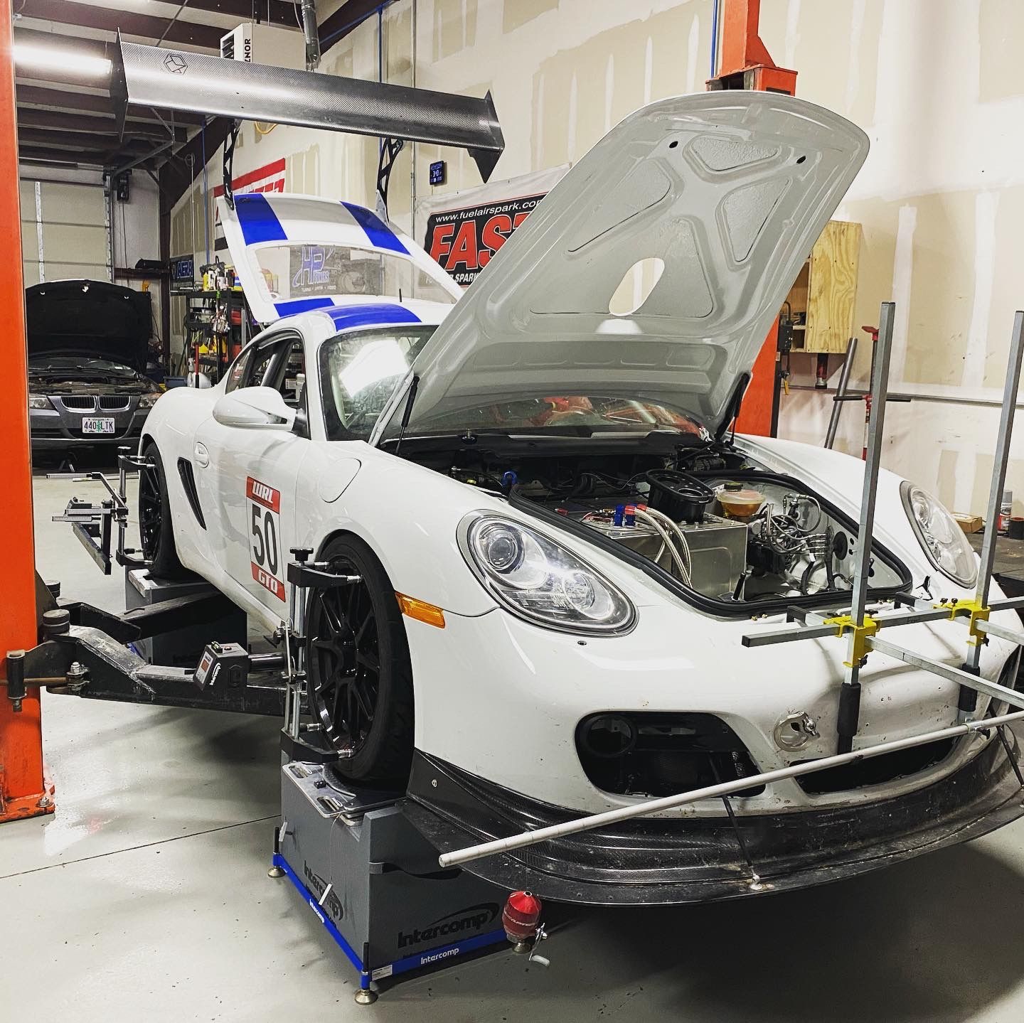 White sports car with hood open on a lift in a garage, being serviced. | YellowHammer Racing