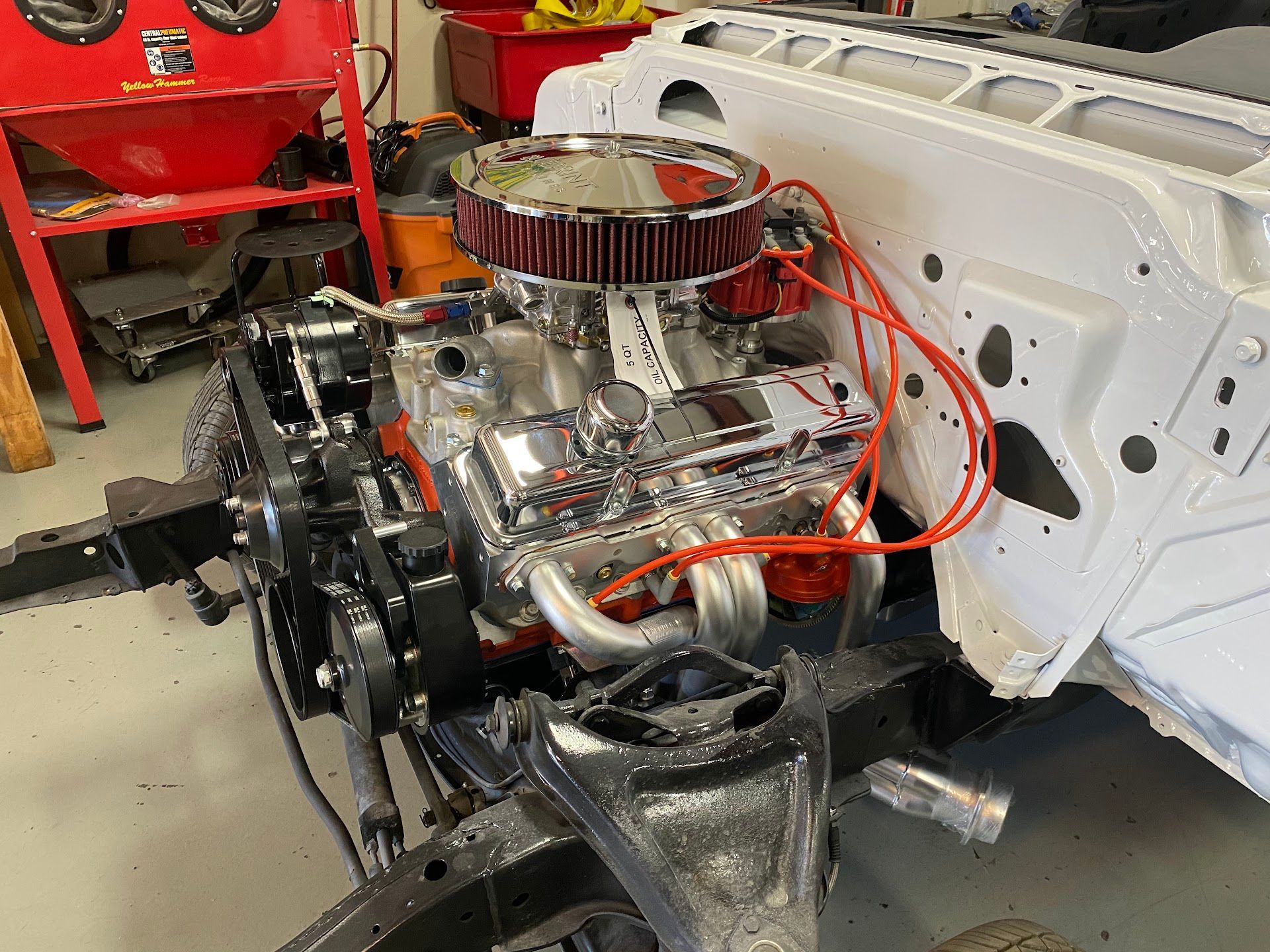 Engine installed in a classic car chassis, bright chrome, white painted frame, shop setting. | YellowHammer Racing