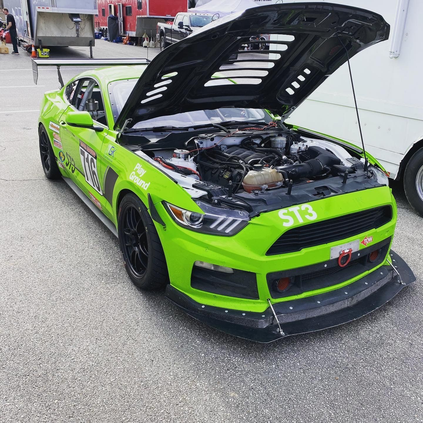 Green race car with hood open, parked on asphalt, 