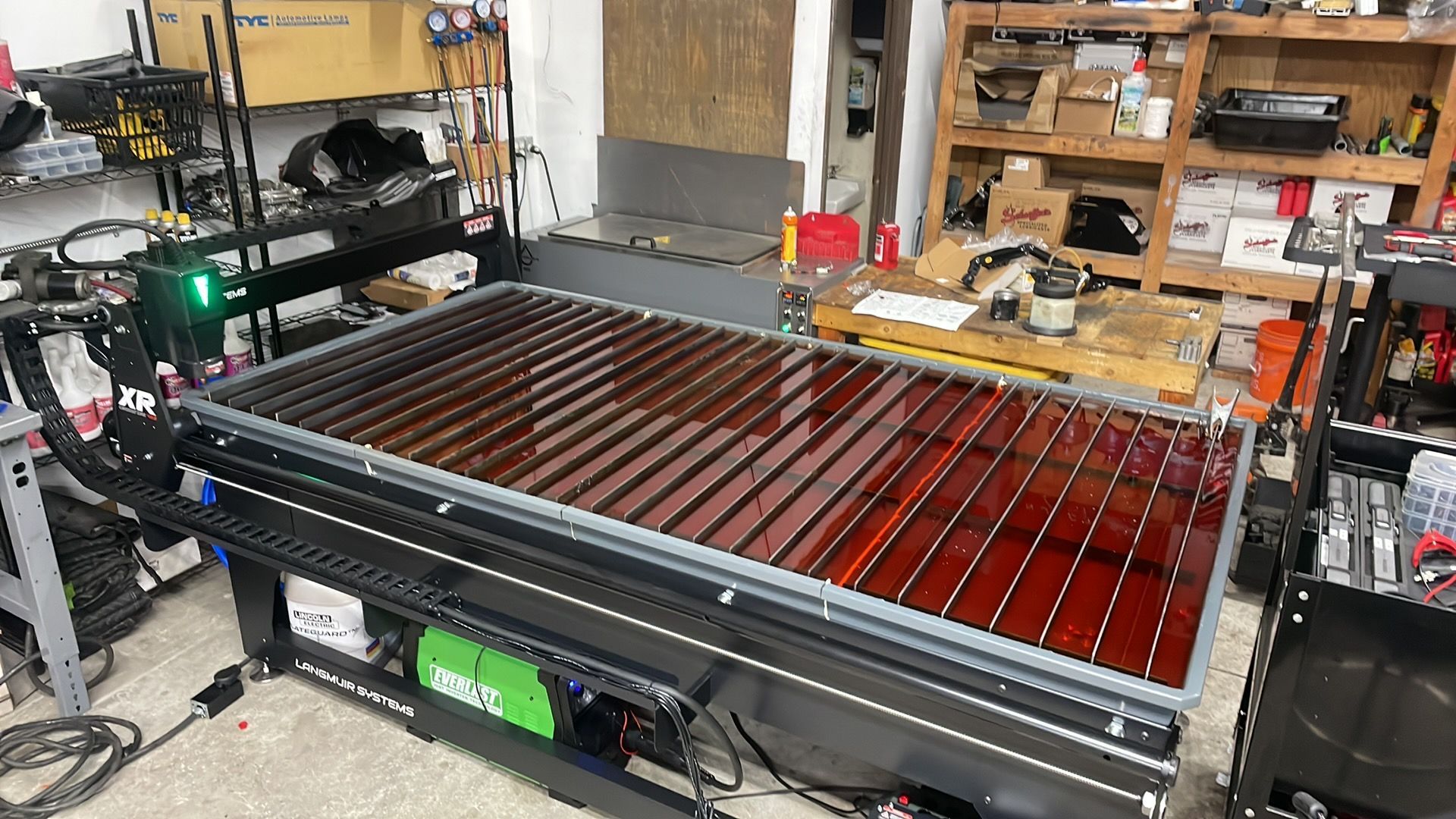 Plasma cutting table with dark water bed, green control box, and equipment in a workshop. | YellowHammer Racing