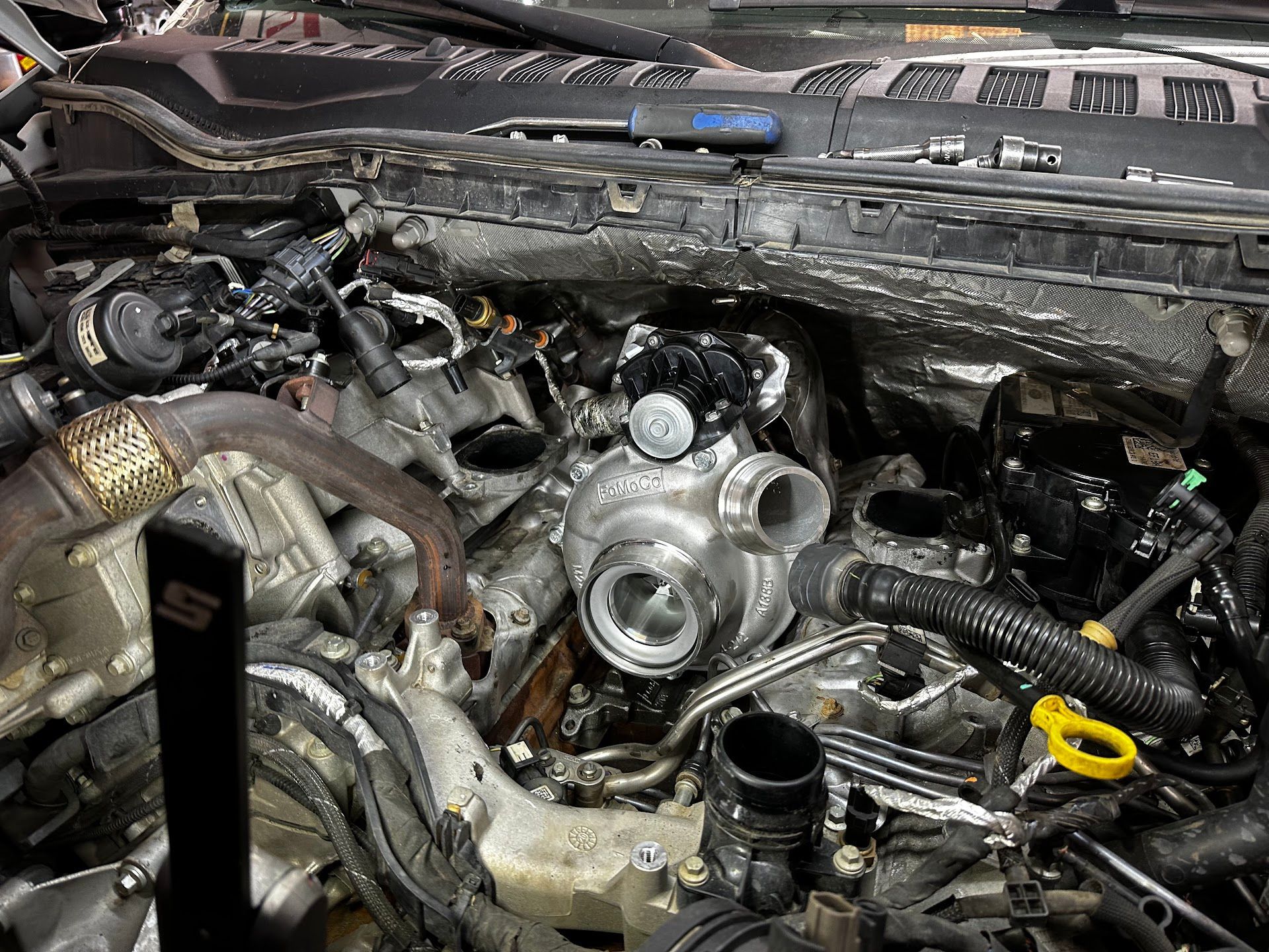 Engine bay, turbocharger installation in progress. Mechanical components visible, some removed. | YellowHammer Racing