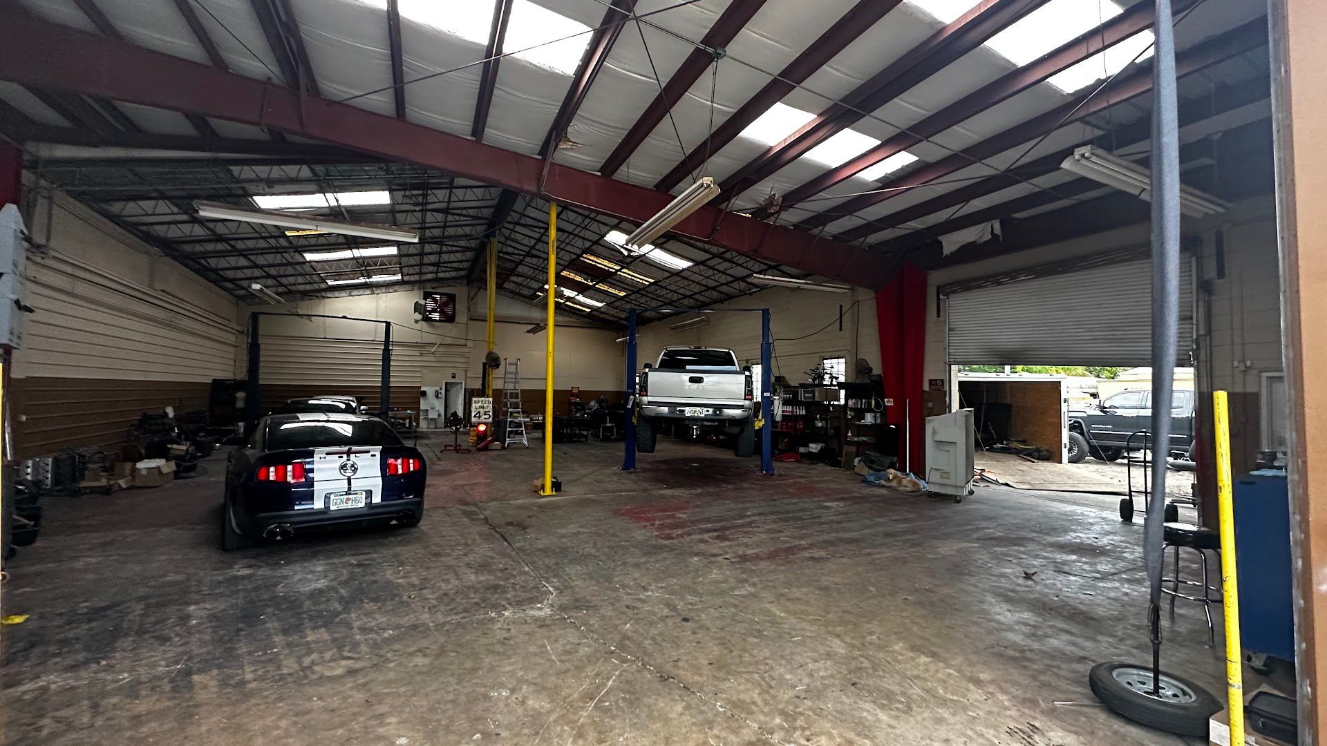 Inside a car repair shop, a black car and white truck on a lift are visible. | YellowHammer Racing