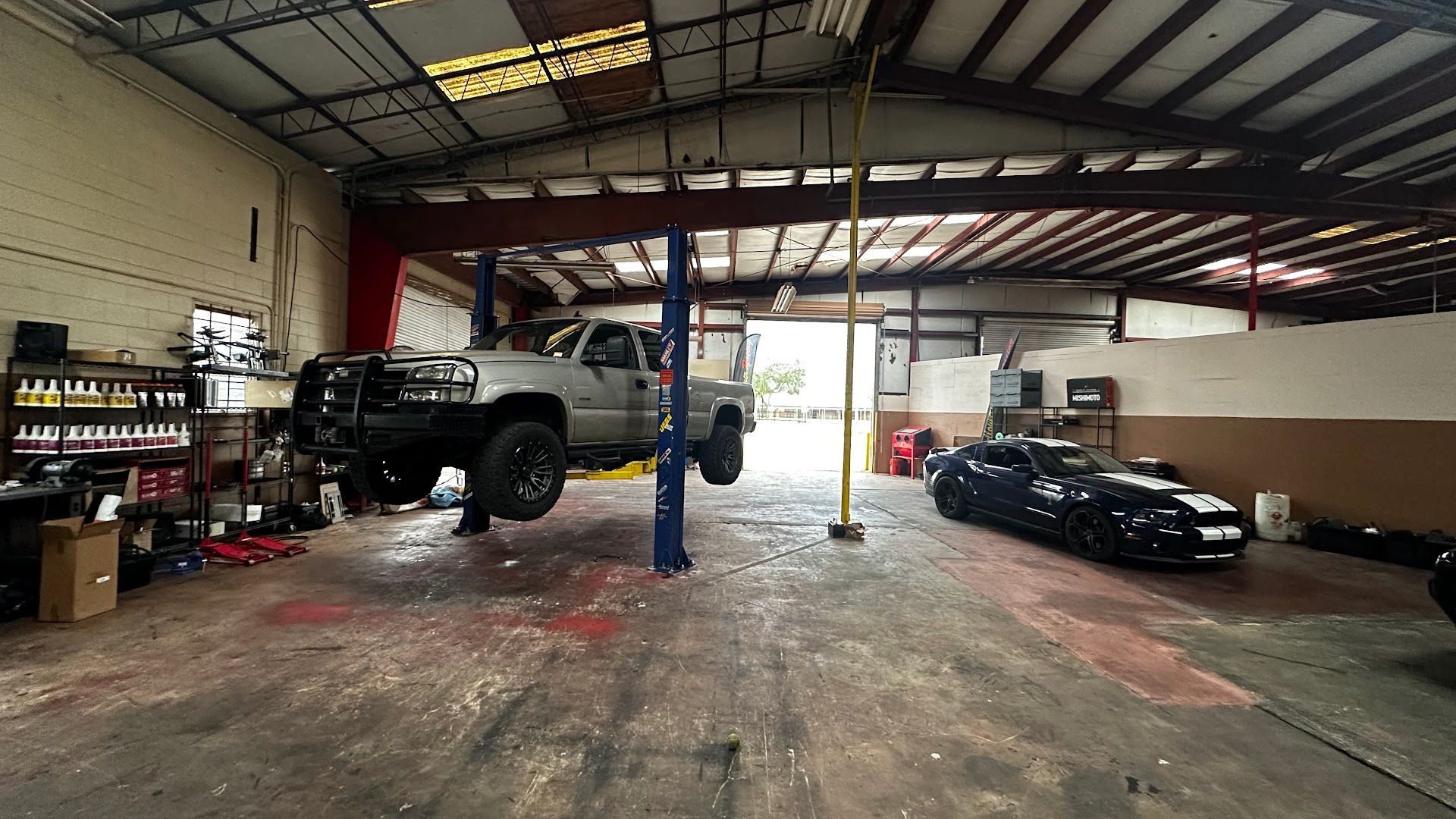 A truck elevated on a lift inside a mechanic's garage. A black car is parked nearby. | YellowHammer Racing