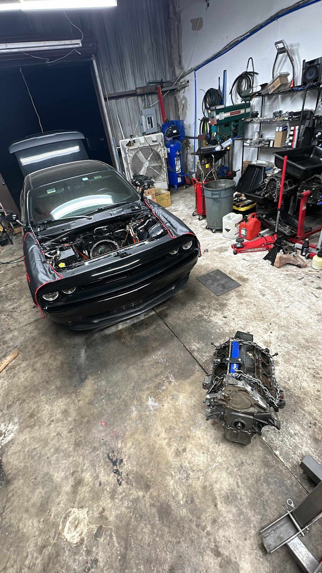 A black Dodge Challenger with the hood up in a garage, engine removed and lying on the ground. | YellowHammer Racing