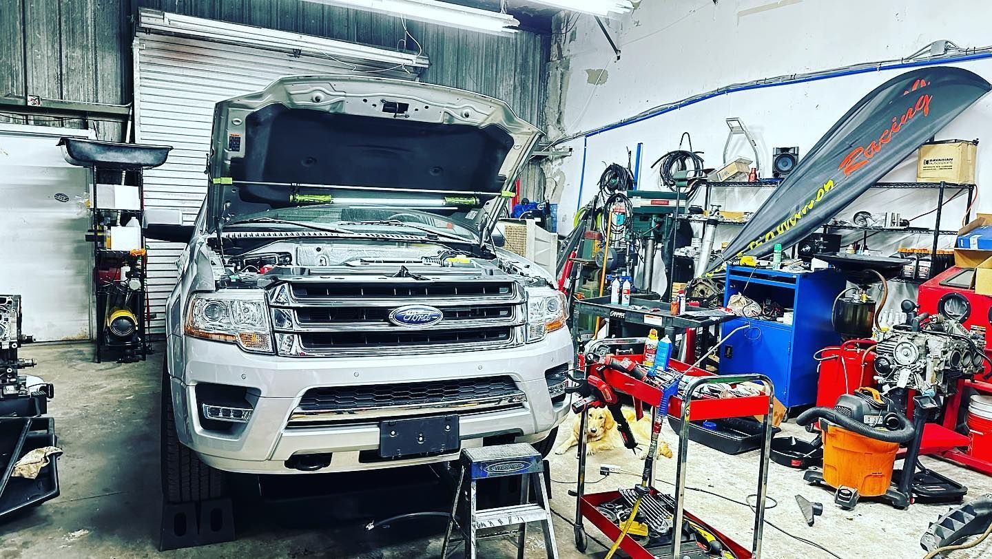 Silver Ford Expedition in a cluttered auto repair shop; hood open, tools visible. | YellowHammer Racing