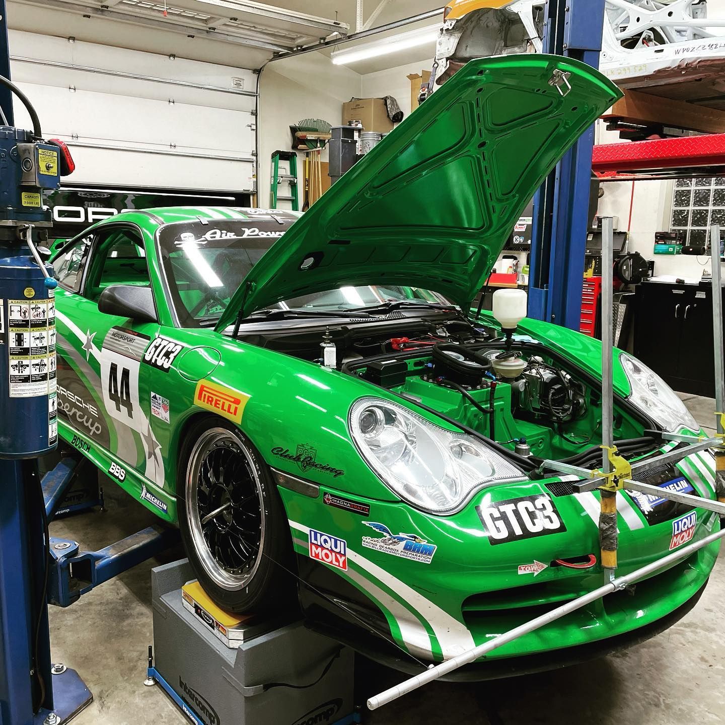 Green racing Porsche on a lift with the hood open in a garage. | YellowHammer Racing