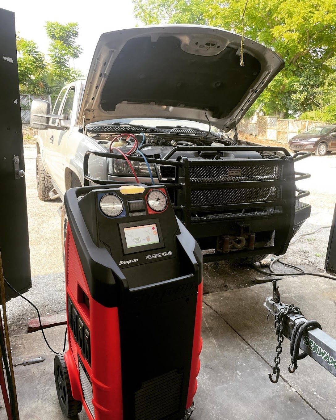 Truck with hood open, connected to a red and black AC machine, outdoors.  | YellowHammer Racing