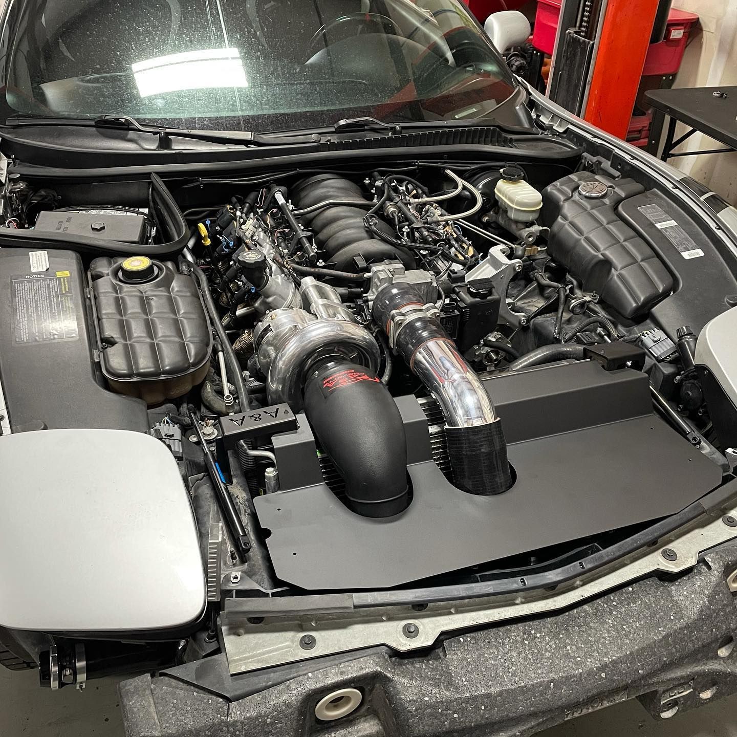 Silver car engine bay with black supercharger, air intake, and components.  | YellowHammer Racing