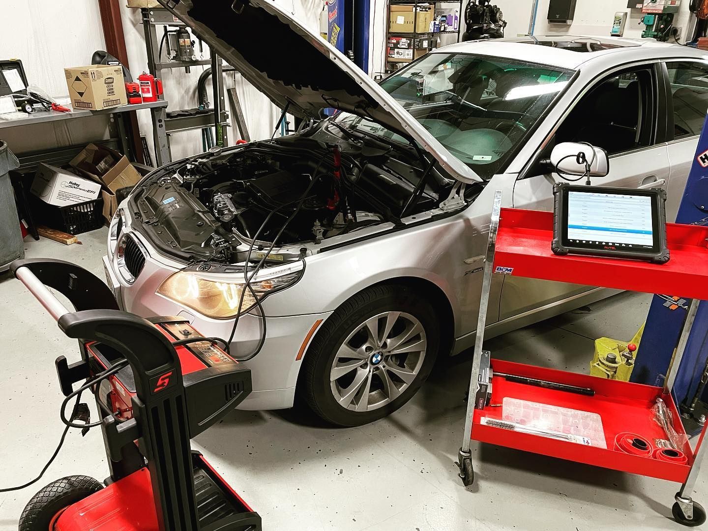 Silver car with open hood in a repair shop, diagnostic equipment nearby, and a tablet on a red cart. | YellowHammer Racing