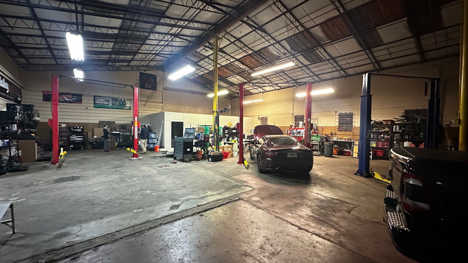 Interior of a car repair shop with cars on lifts, tools, and equipment scattered around.  | YellowHammer Racing
