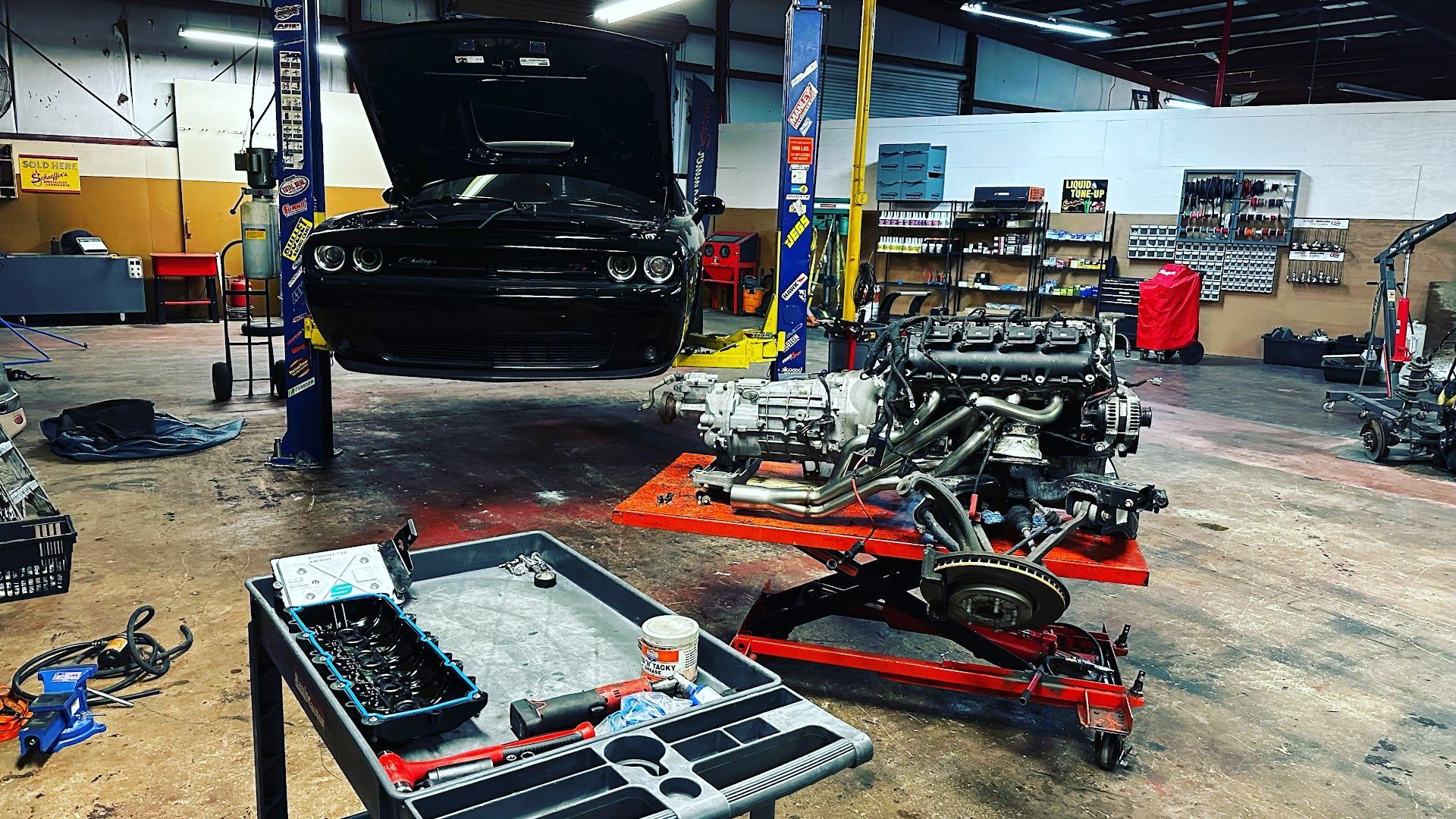 Black car raised on a lift in a garage, engine nearby on a cart, tools on a table. | YellowHammer Racing