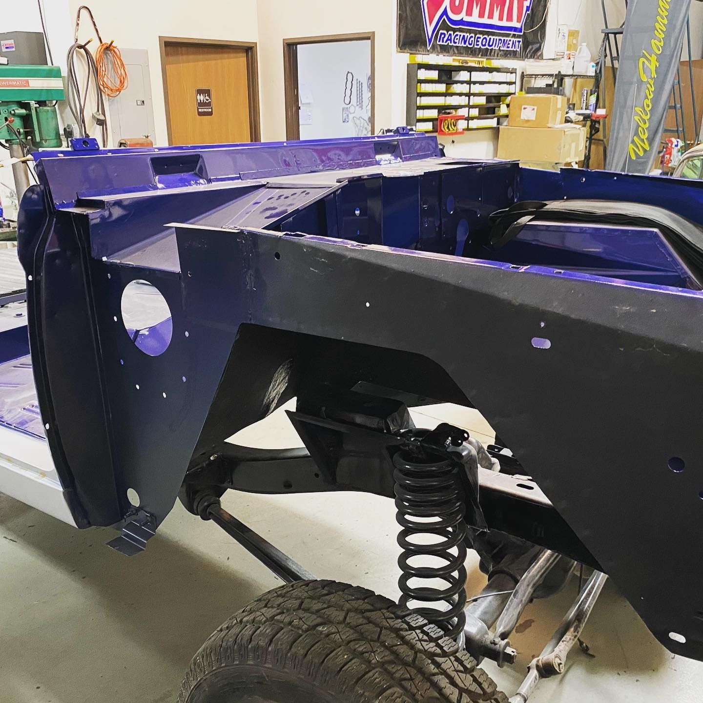 Blue and black vehicle frame under construction in a workshop, showing suspension and tire. | YellowHammer Racing