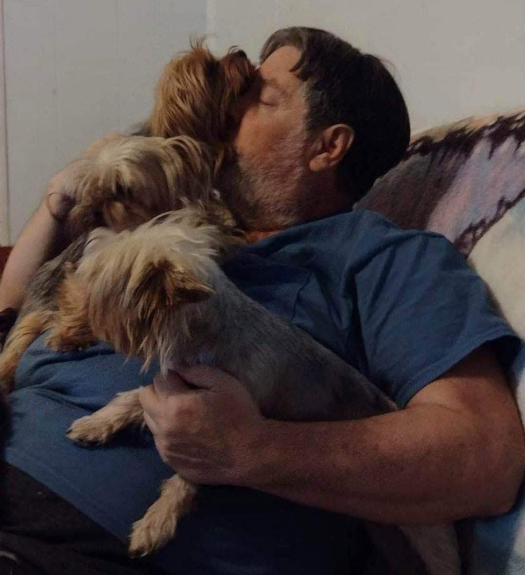 Woman on couch kissing two small dogs while holding one in her arms
