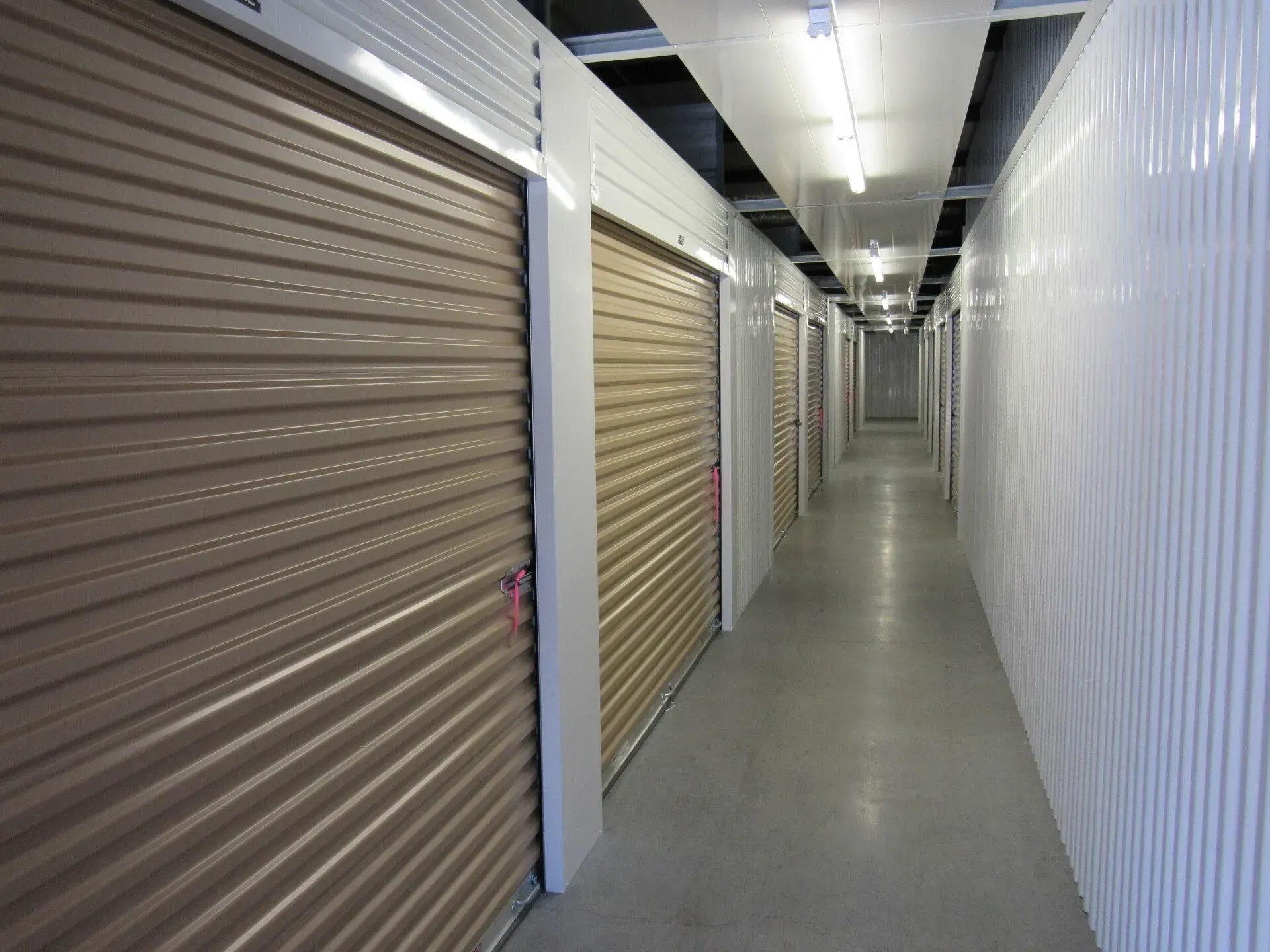 Storage unit hallway with closed beige doors and a long white wall.