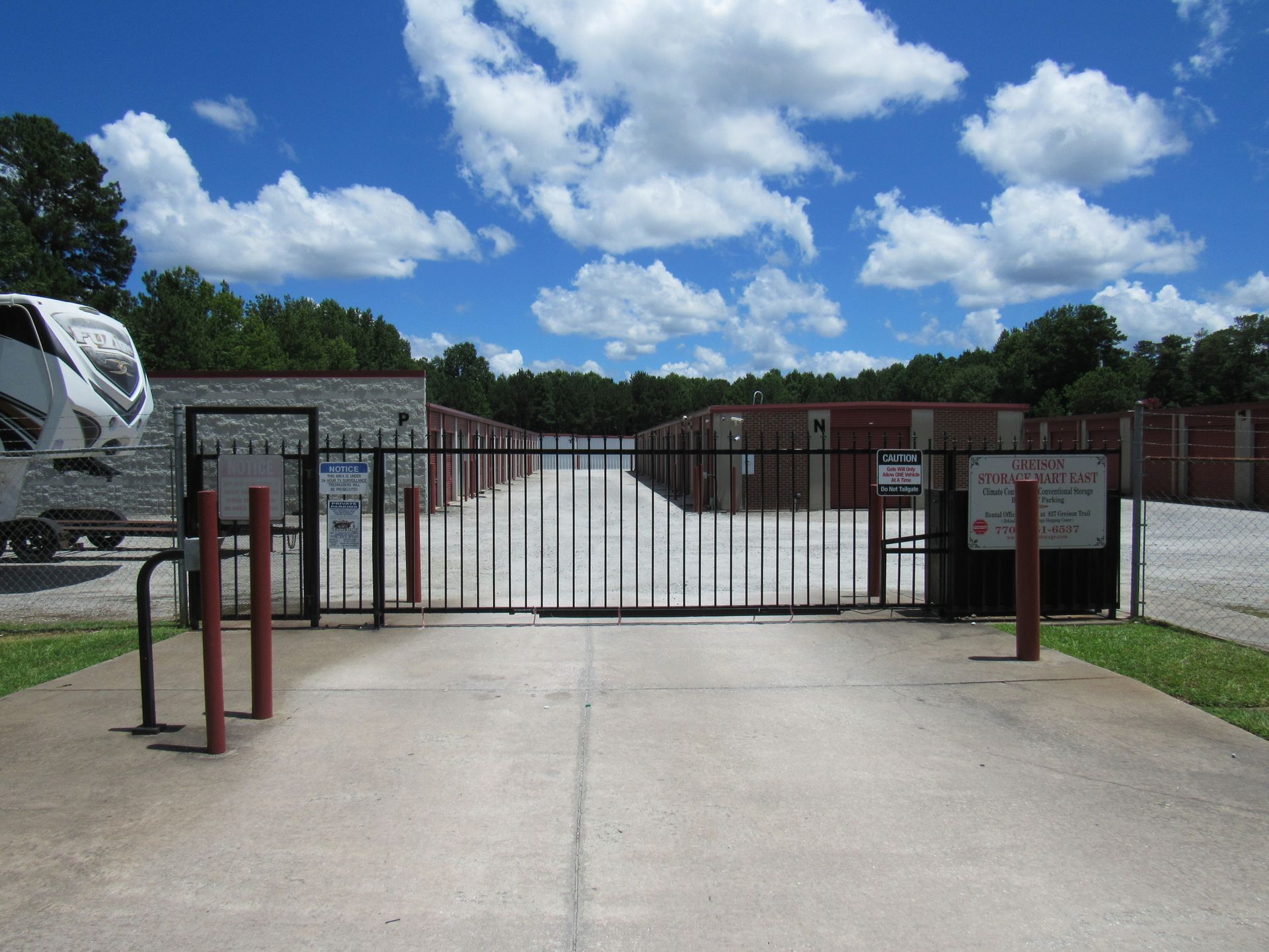 Gated storage facility with red and black gate posts under a blue sky with fluffy white clouds.