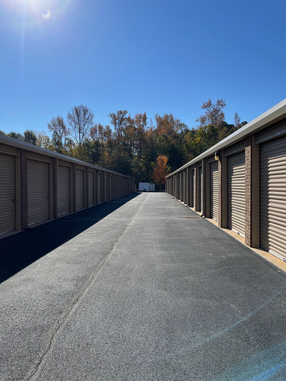 Rows of storage units with closed metal doors, asphalt path, sunny day.