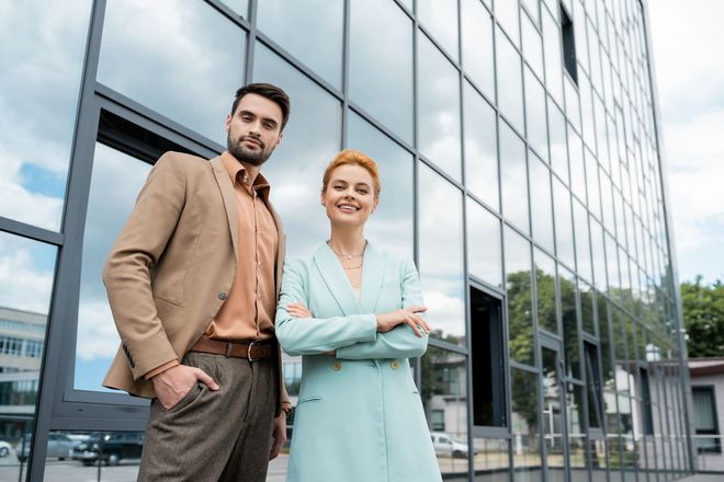 A smiling couple posing outdoors in front of a building.