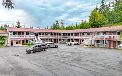 Motel exterior with red doors and roof, vehicles parked in front, surrounded by trees.
