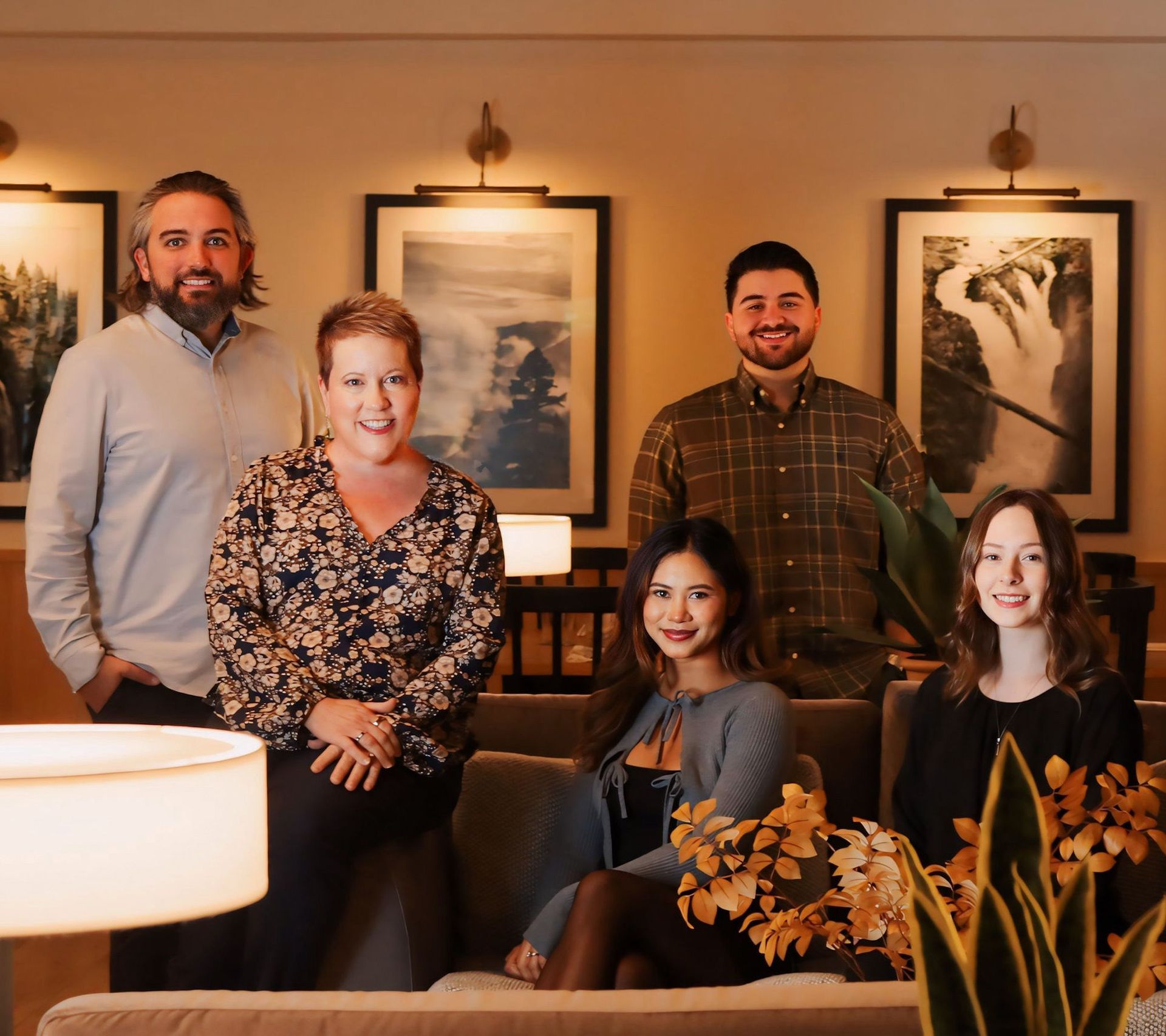 Group of people posing indoors in front of paintings, seated on a couch.