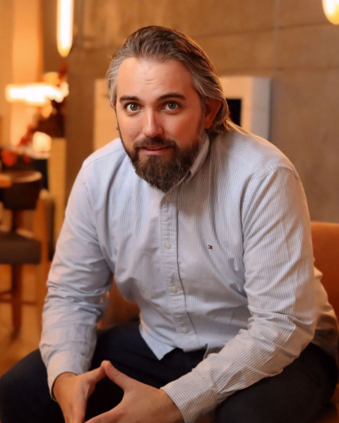 Man with beard smiles, wearing a gray button-down shirt.