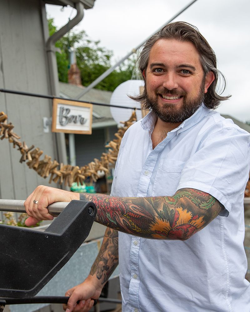 Man with tattoos, smiling, holding a railing outside a