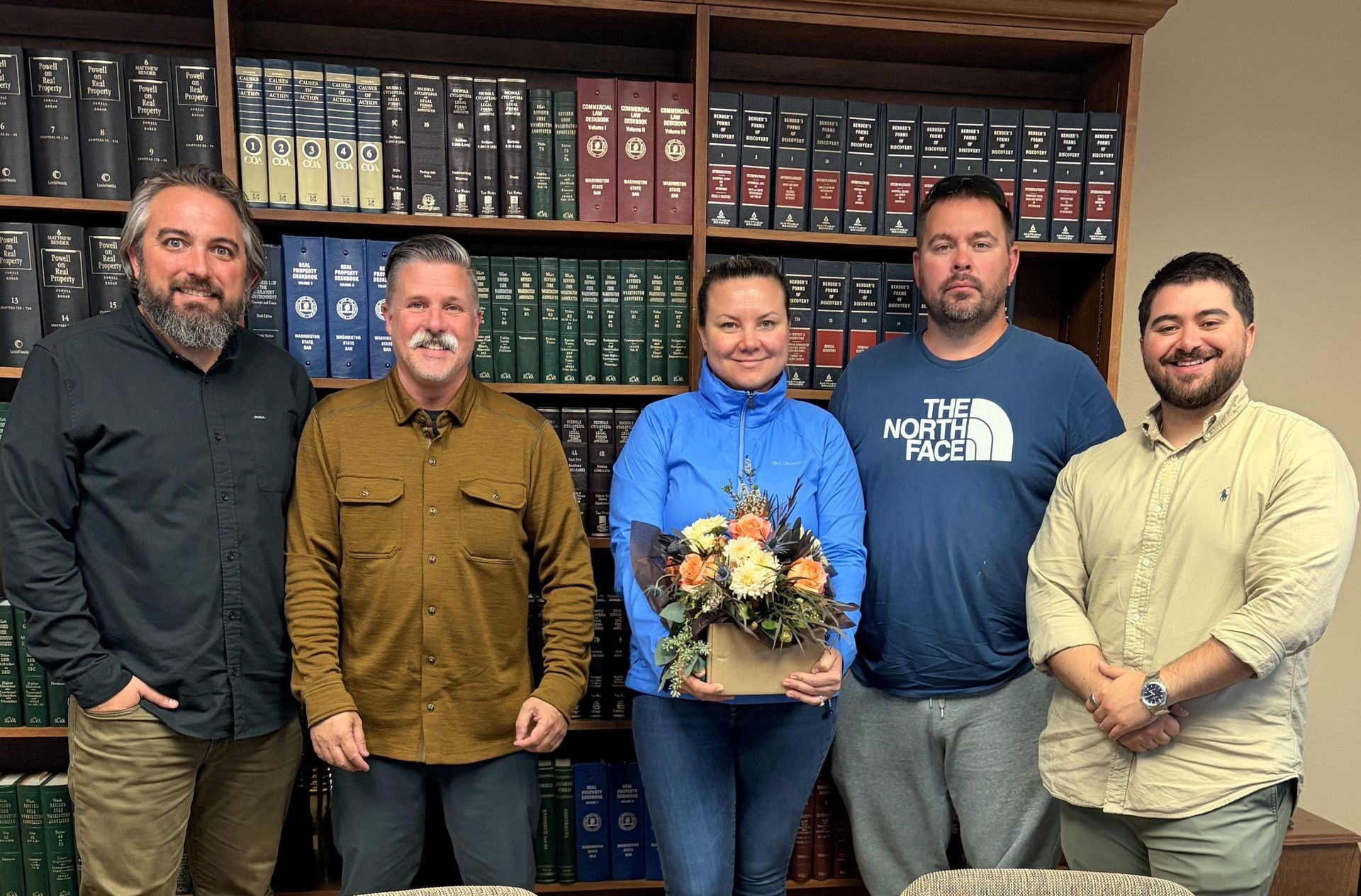 Five people standing in front of bookshelves, holding flowers.