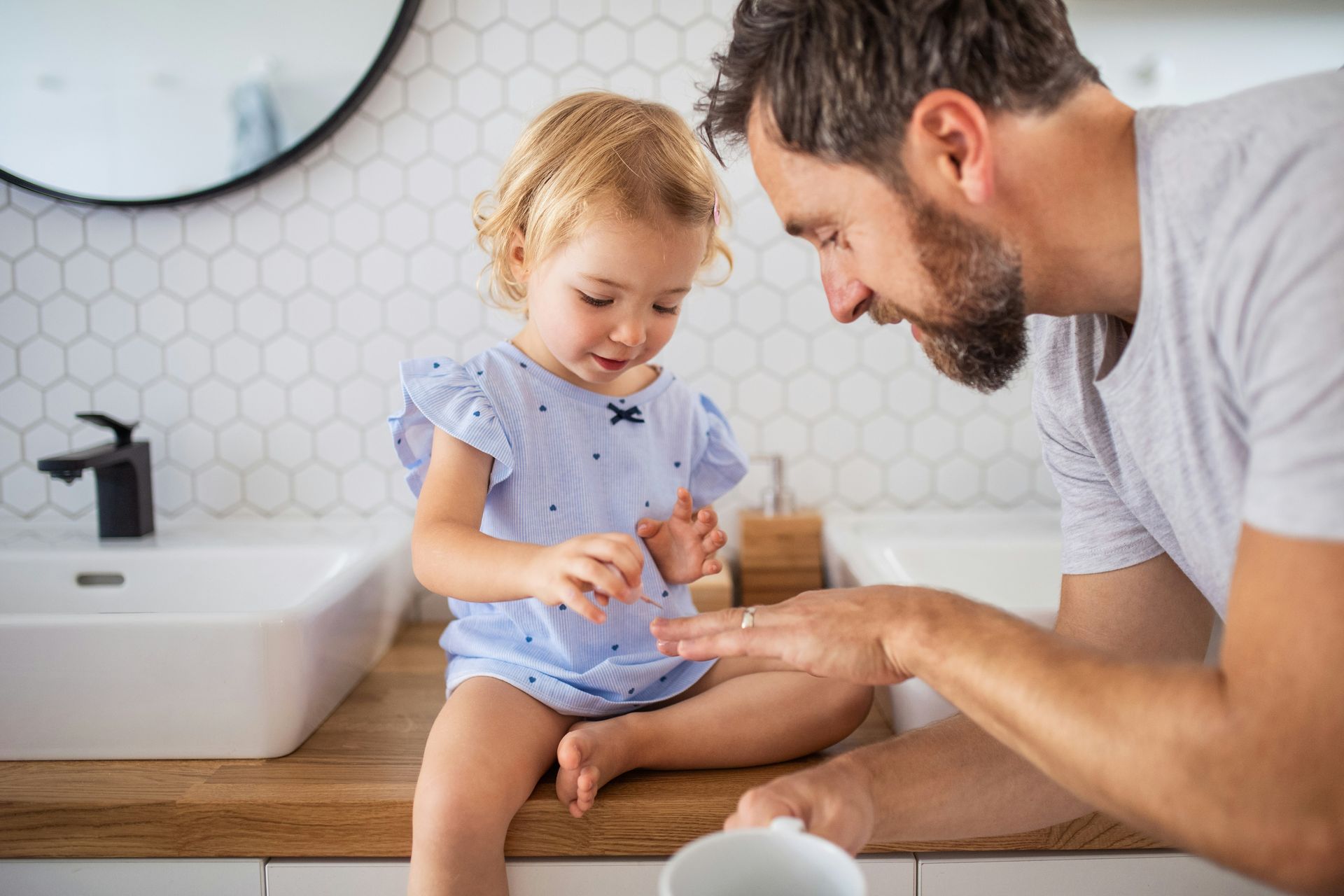 Man and child in a bathroom, looking at a hand. The child is sitting on the counter.