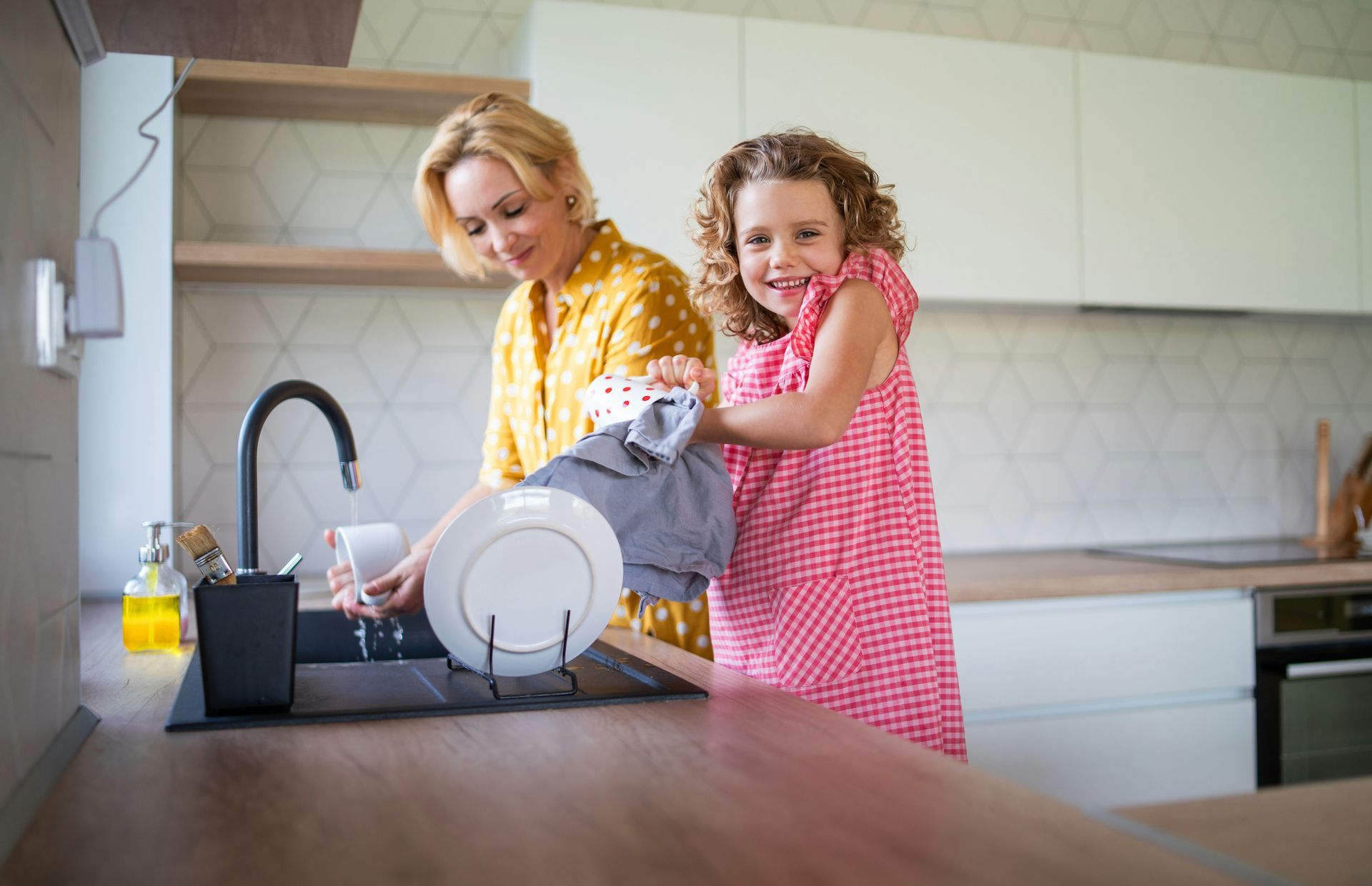 Woman and child washing dishes together in a modern kitchen.