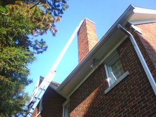 Roofing worker on a ladder repairing a brick house chimney against a blue sky