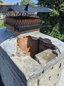 Damaged brick chimney with a metal cap and broken concrete crown on a rooftop